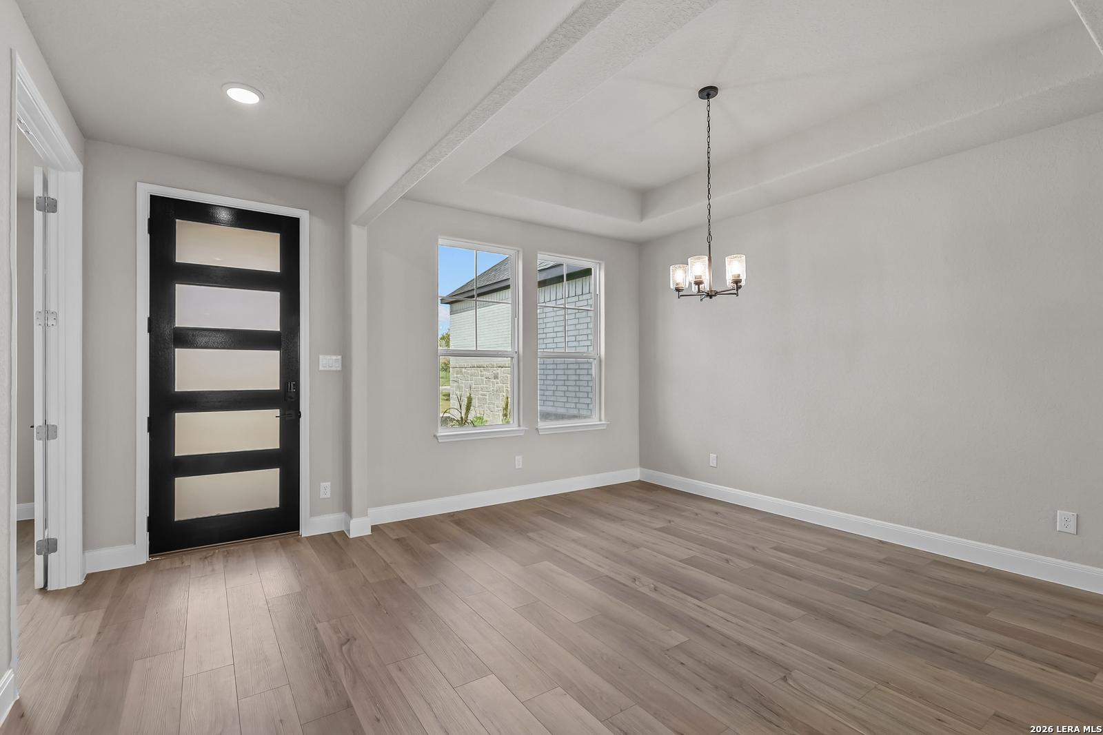 Bright dining room with wood-look flooring, black front door, and chandelier in Davidson Homes The Foster E, Castroville, Texas