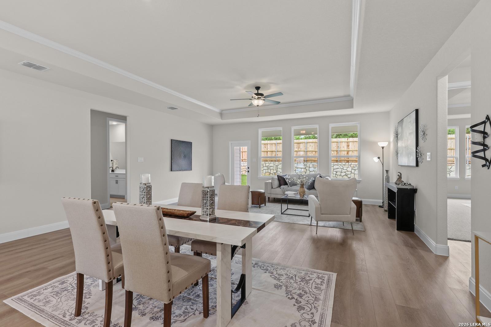 Spacious open dining and living area with farmhouse table, gray sofa, and backyard views in The Lanier G home, Castroville, Texas