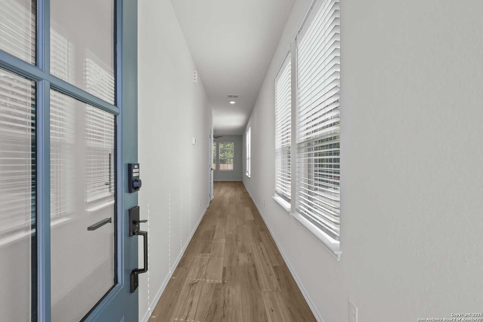 Bright entry hallway with light wood floors and window blinds in Davidson Homes The Florence C, San Antonio