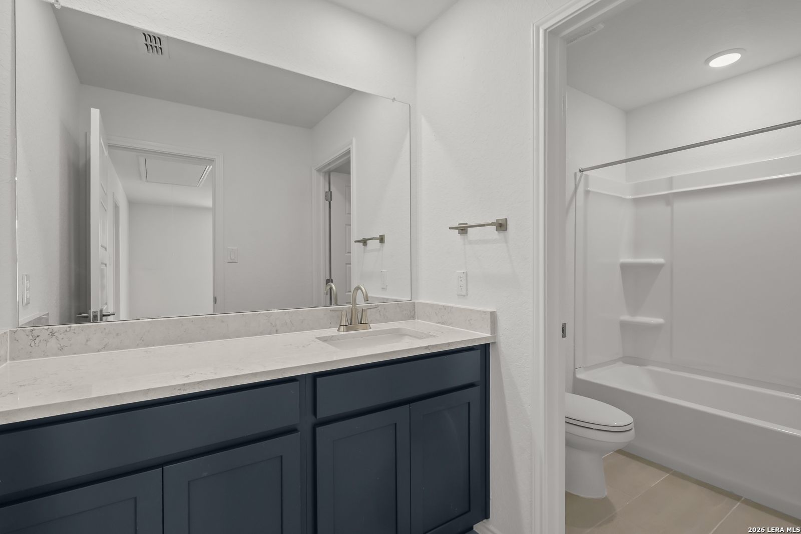 Modern bathroom with dark navy vanity, stone countertop, and shower-tub combo in The Gillian C home, Meadows at Oak Creek.