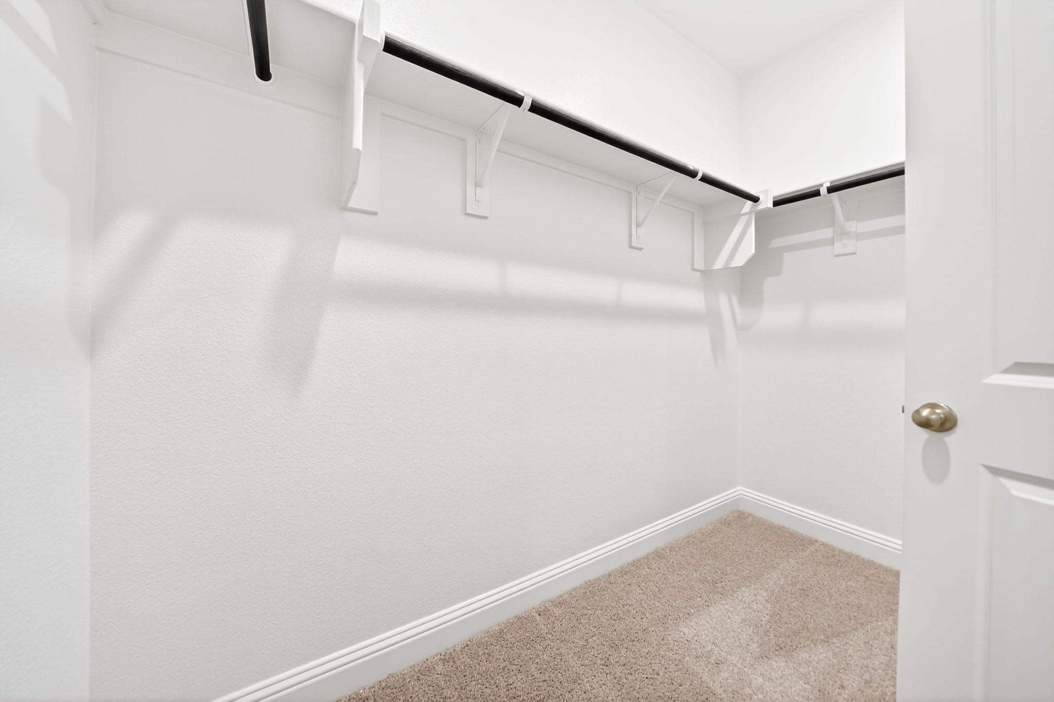 Spacious walk-in closet in the Redbud master suite featuring white walls, carpeting, and overhead shelving and rods.