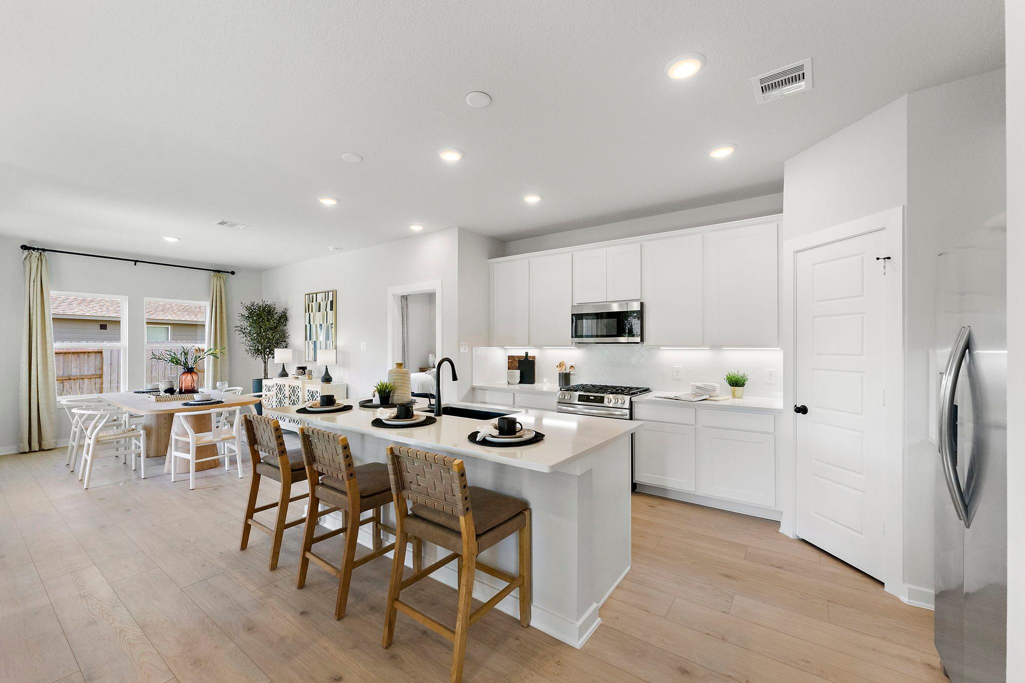 Modern open-concept kitchen in Sundance Cove, Crosby, Texas with white cabinets, large island, wooden bar stools, and hardwood floors