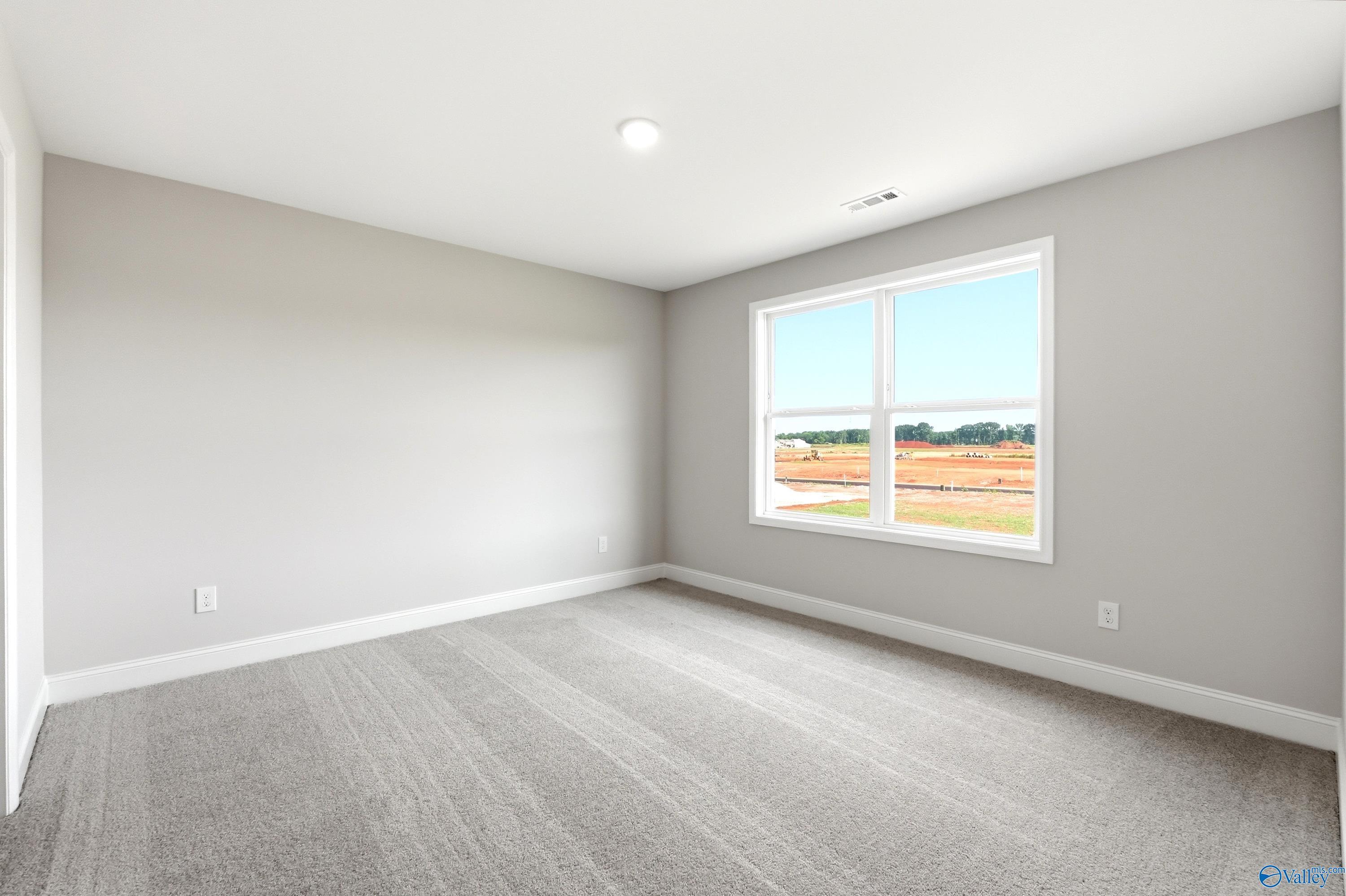 Bright, spacious secondary bedroom with neutral carpet and large window in The Shelby A floor plan, Hazel Green, Alabama.