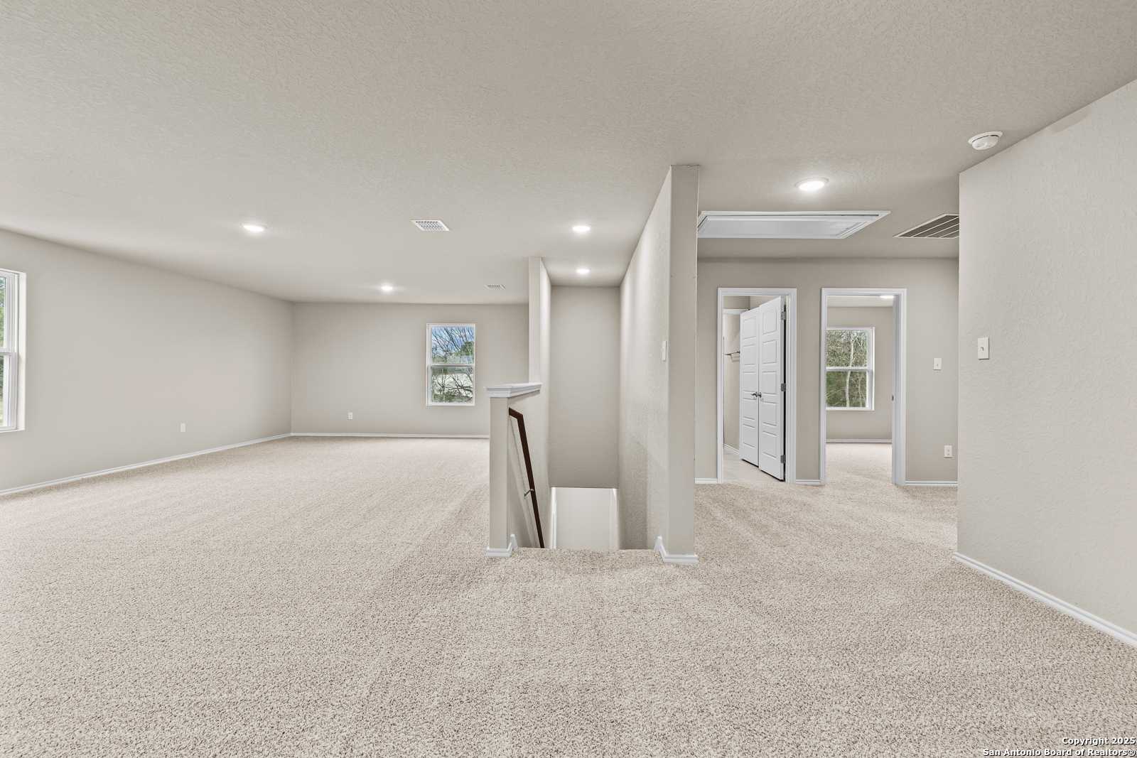 Spacious upstairs loft with beige carpet, bedroom doors, and overlook railing in Davidson Homes The Douglas F, San Antonio