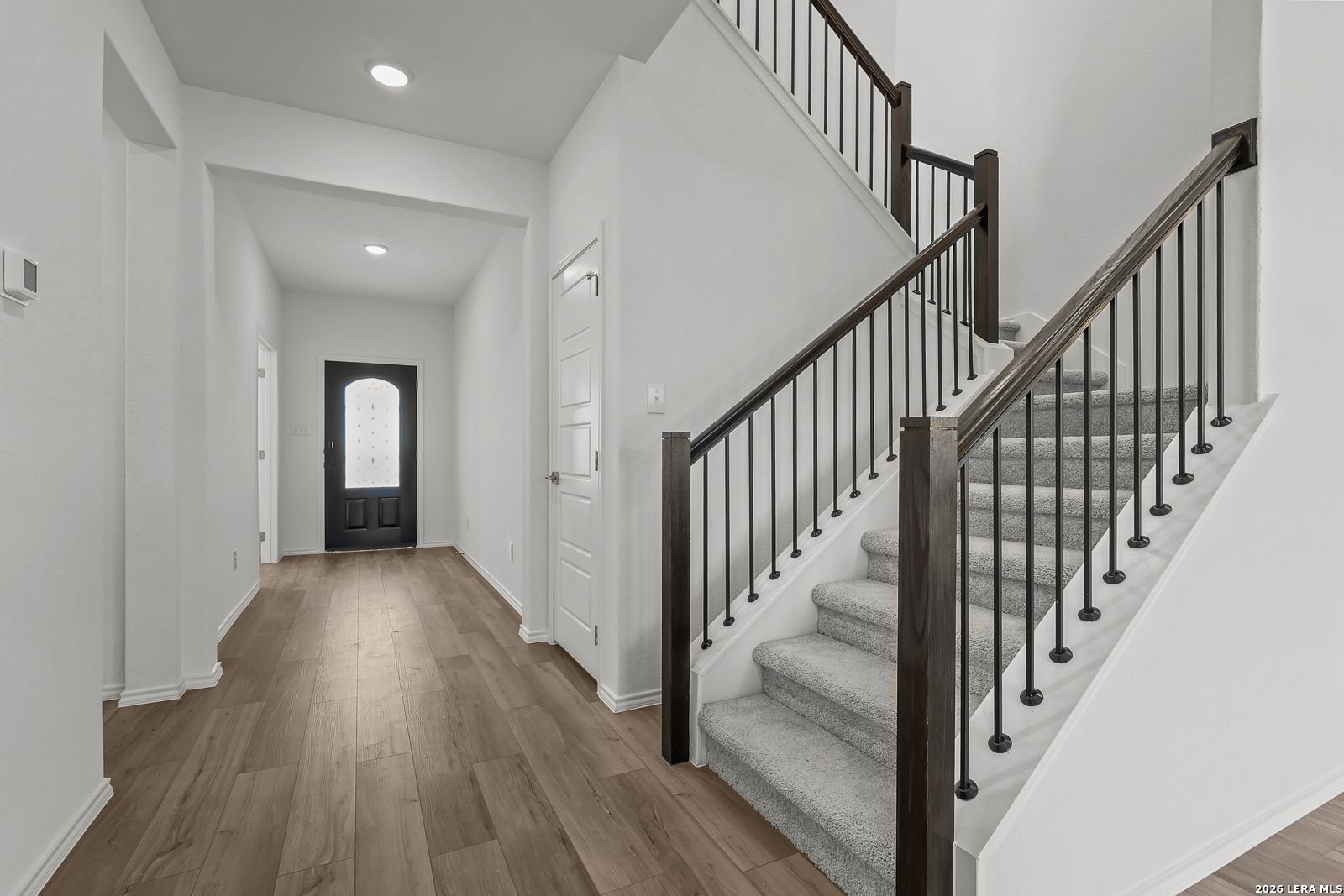 Elegant entry hallway with sweeping staircase, arched black door, and wood floors in Davidson Homes Sequoia B, San Antonio