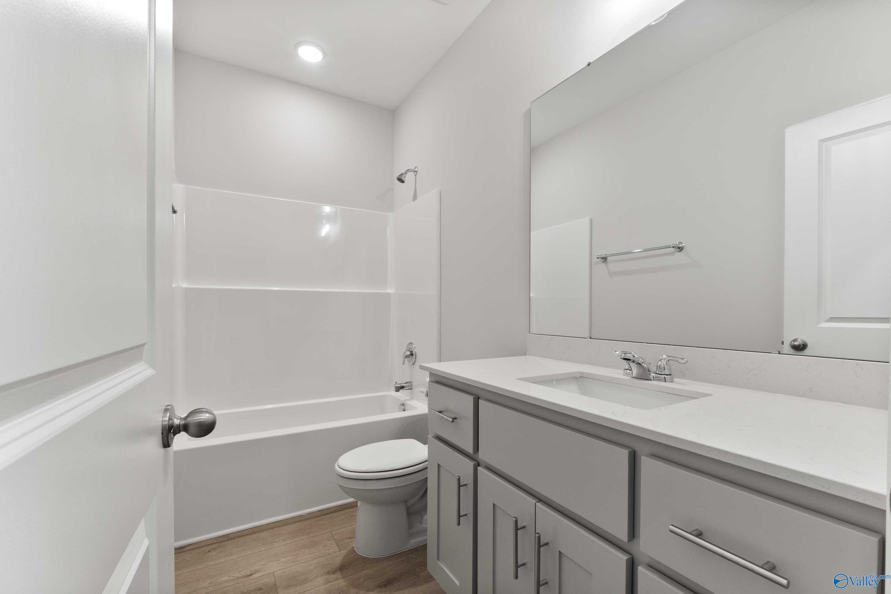 Modern white bathroom with tub-shower combo, double vanity sink, mirror, and wood floors in Davidson Homes The Daphne C, Athens AL