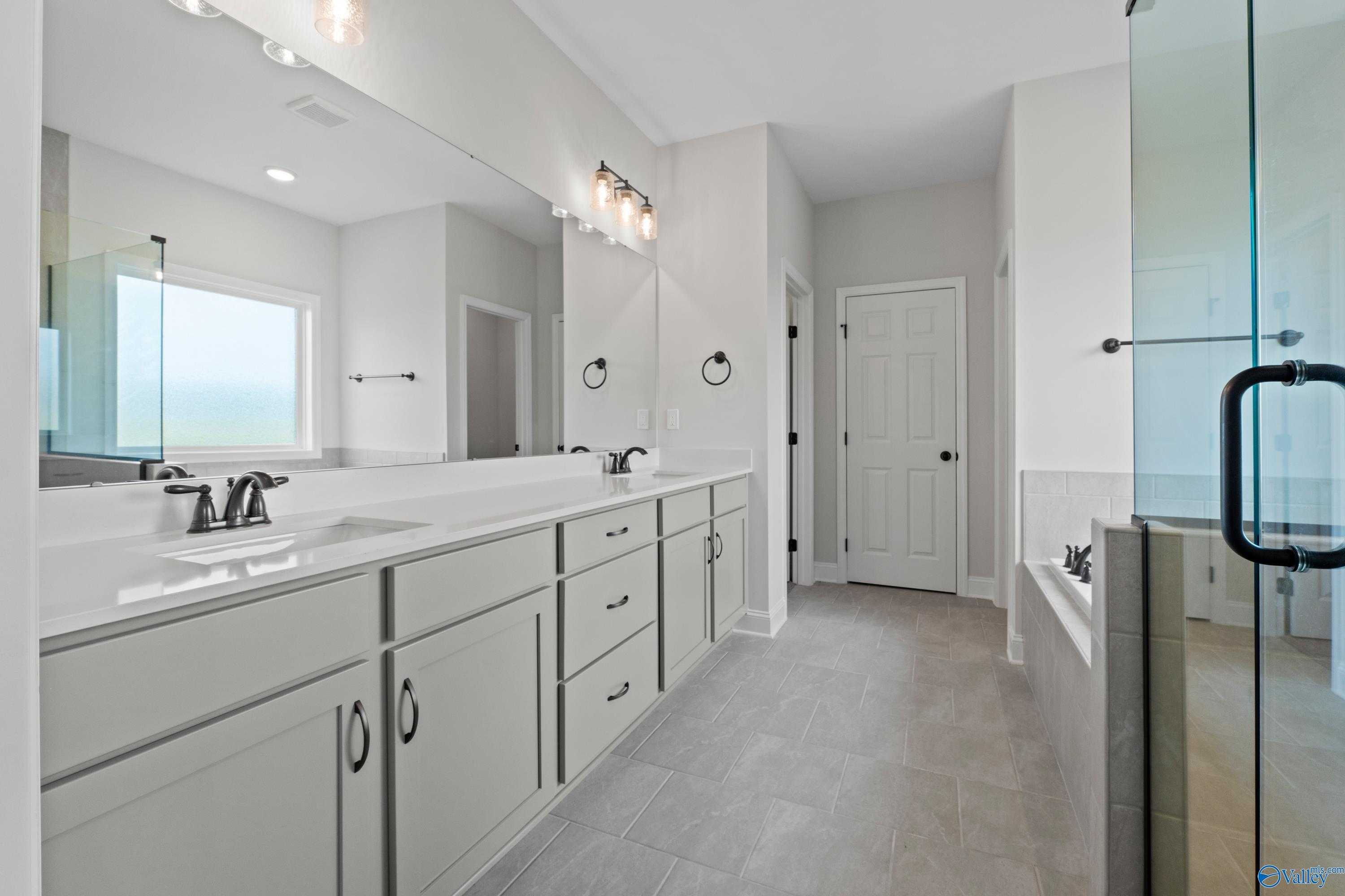 Spacious master bathroom with double vanity, glass shower, soaking tub, and white cabinets in Davidson Homes The Kirkland, Harvest, AL