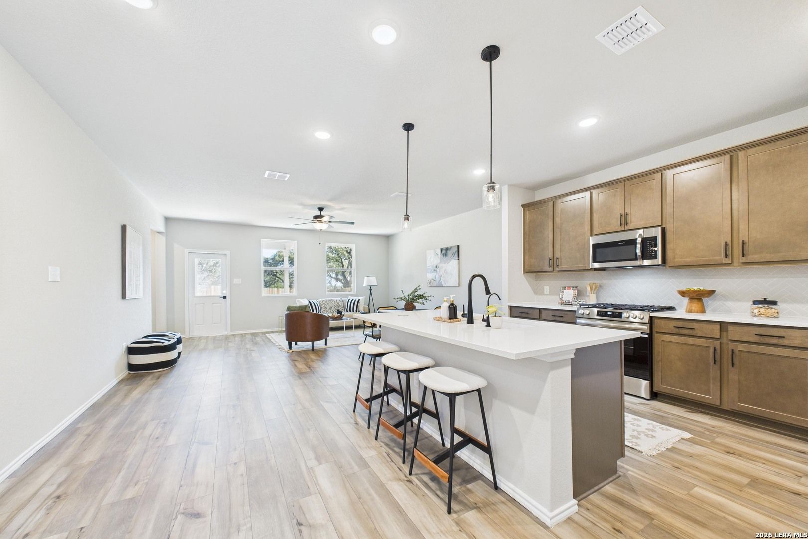 Open-concept kitchen and living room with quartz island, bar stools, hardwood floors, and stainless appliances in Davidson Homes The Douglas E, San Antonio
