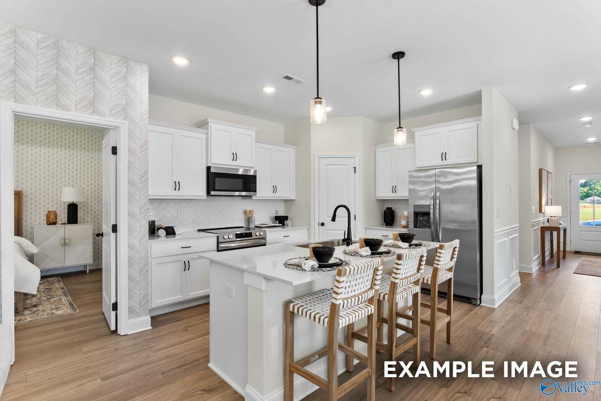 Modern white kitchen island with bar stools, stainless appliances, pendant lights in Davidson Homes The Franklin, Huntsville AL