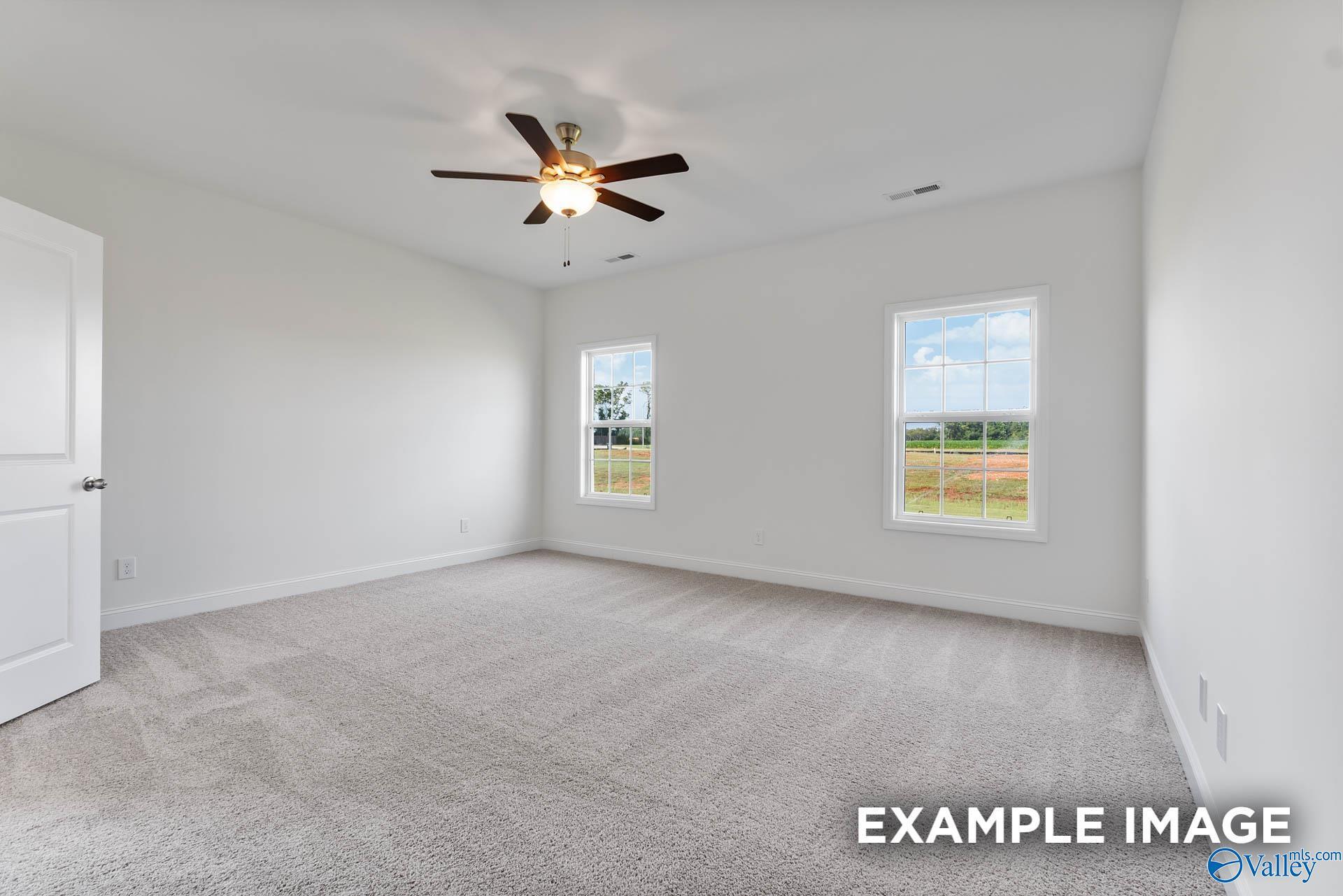 Bright bedroom with white walls, beige carpet, ceiling fan, and large windows in Davidson Homes The Harrison C, Athens, Alabama