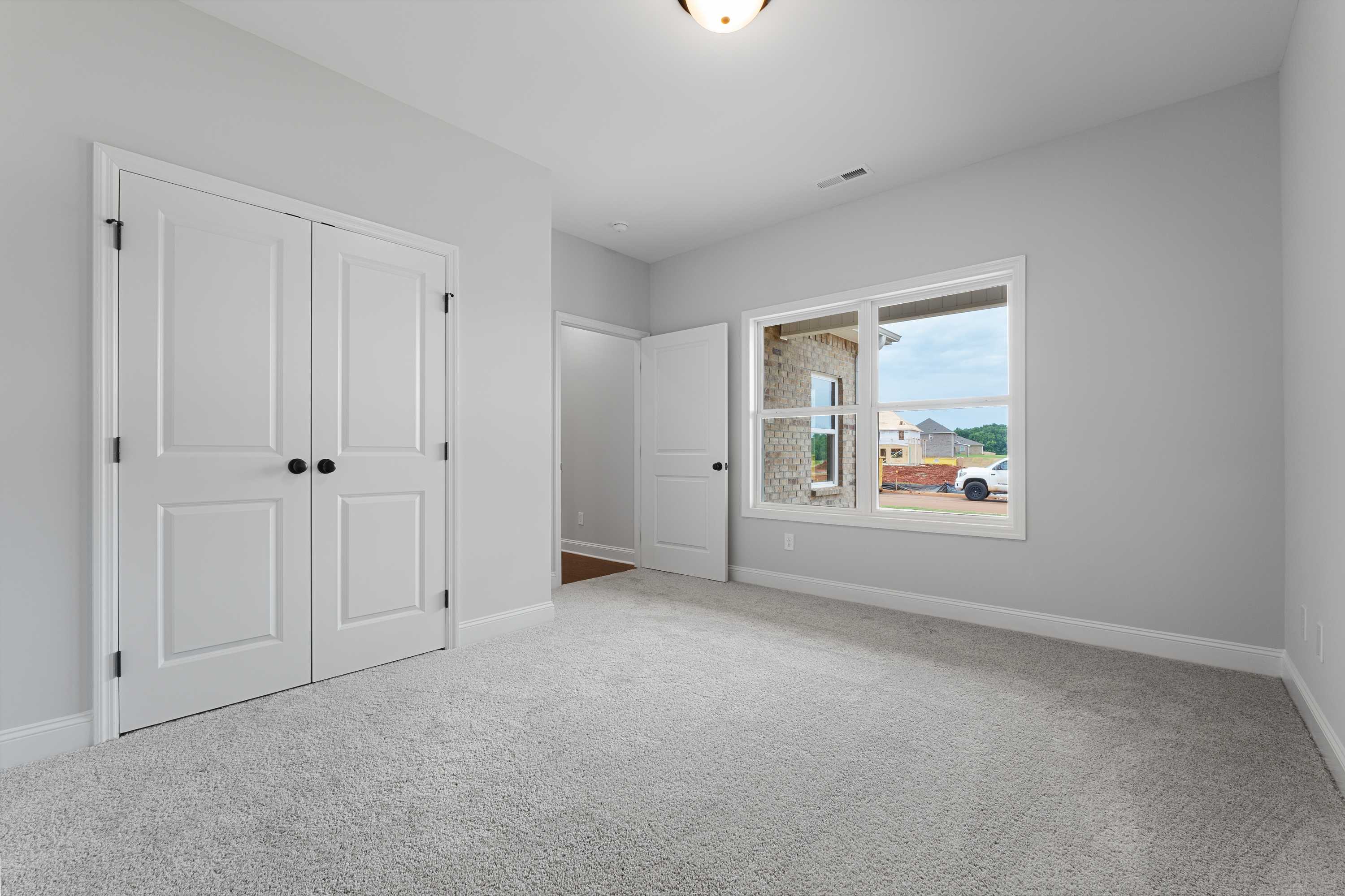 Spacious secondary bedroom in The Copeland by Davidson Homes, Madison AL, with gray walls, white double doors, carpet floor, large window