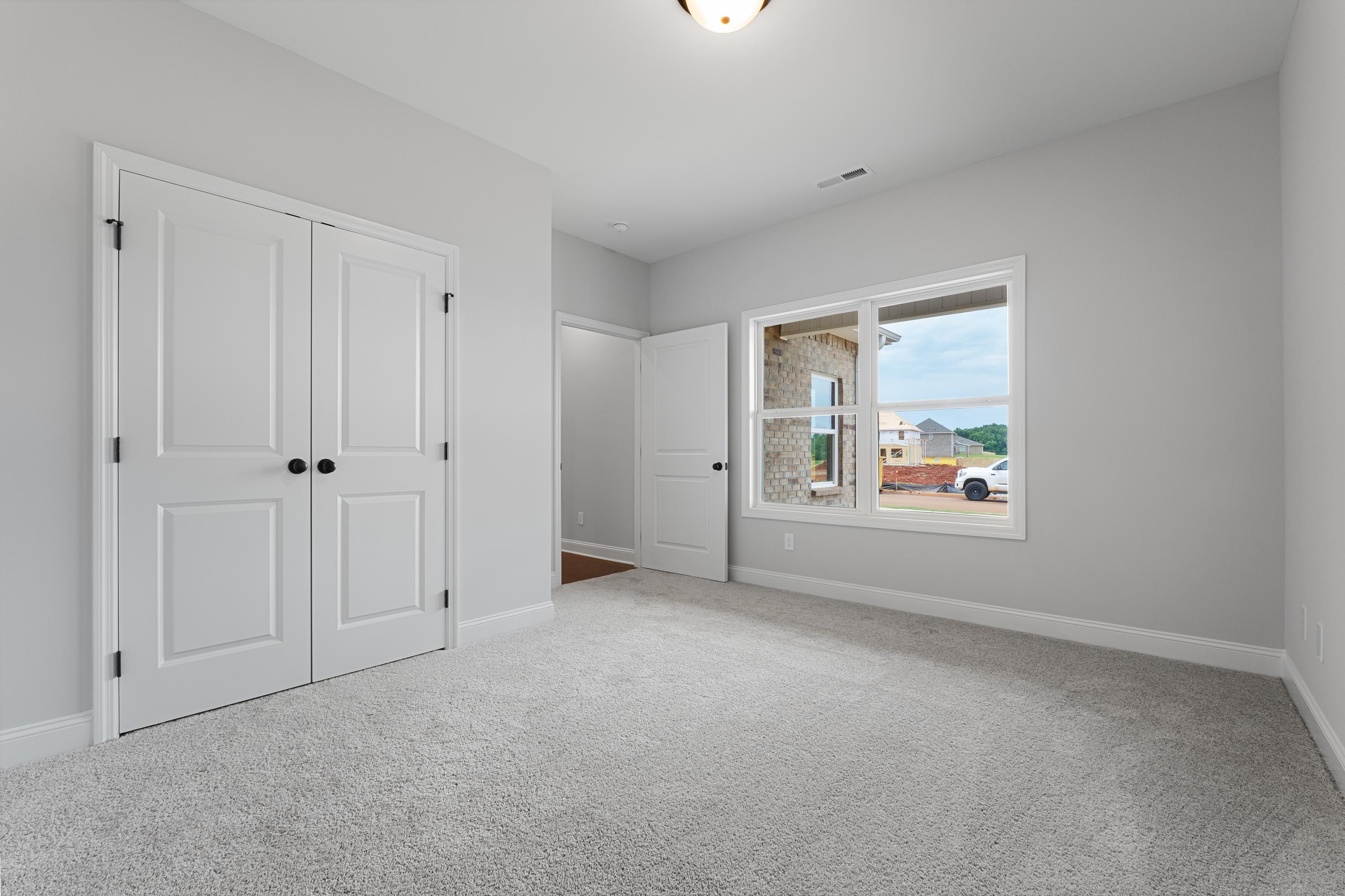 Spacious secondary bedroom in The Copeland by Davidson Homes, Madison AL, with gray walls, white double doors, carpet floor, large window
