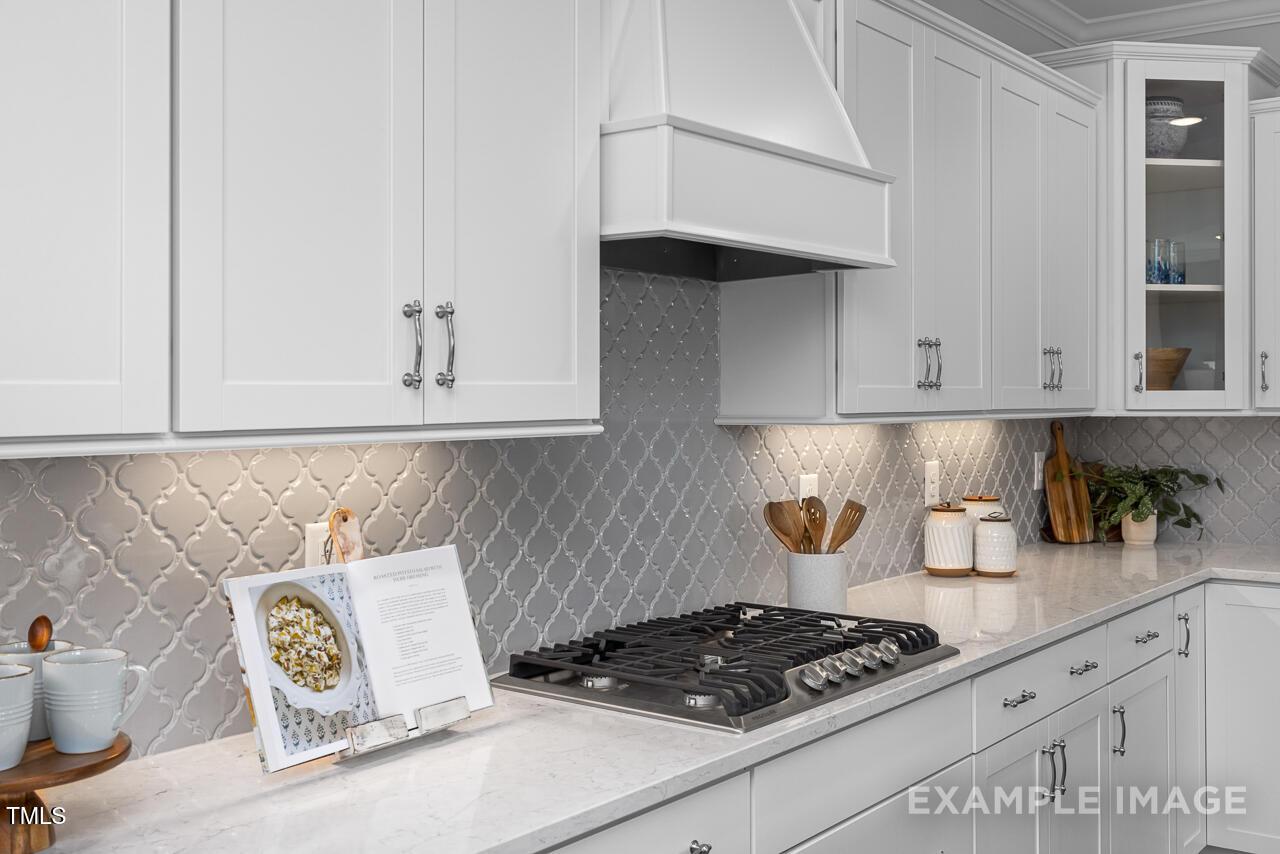 Modern white shaker kitchen with herringbone gray tile backsplash, quartz counters, gas range in Davidson Homes Magnolia B, Angier, NC