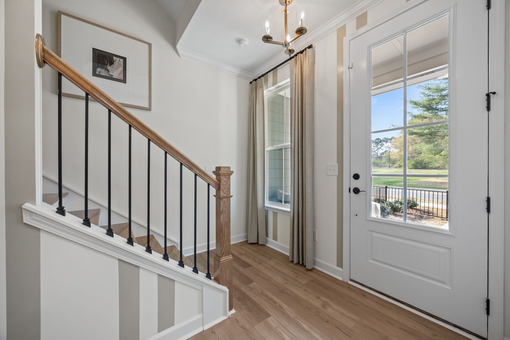 Bright foyer entrance of The Mitchell design featuring a modern staircase, wood flooring, and elegant glass-paneled door.