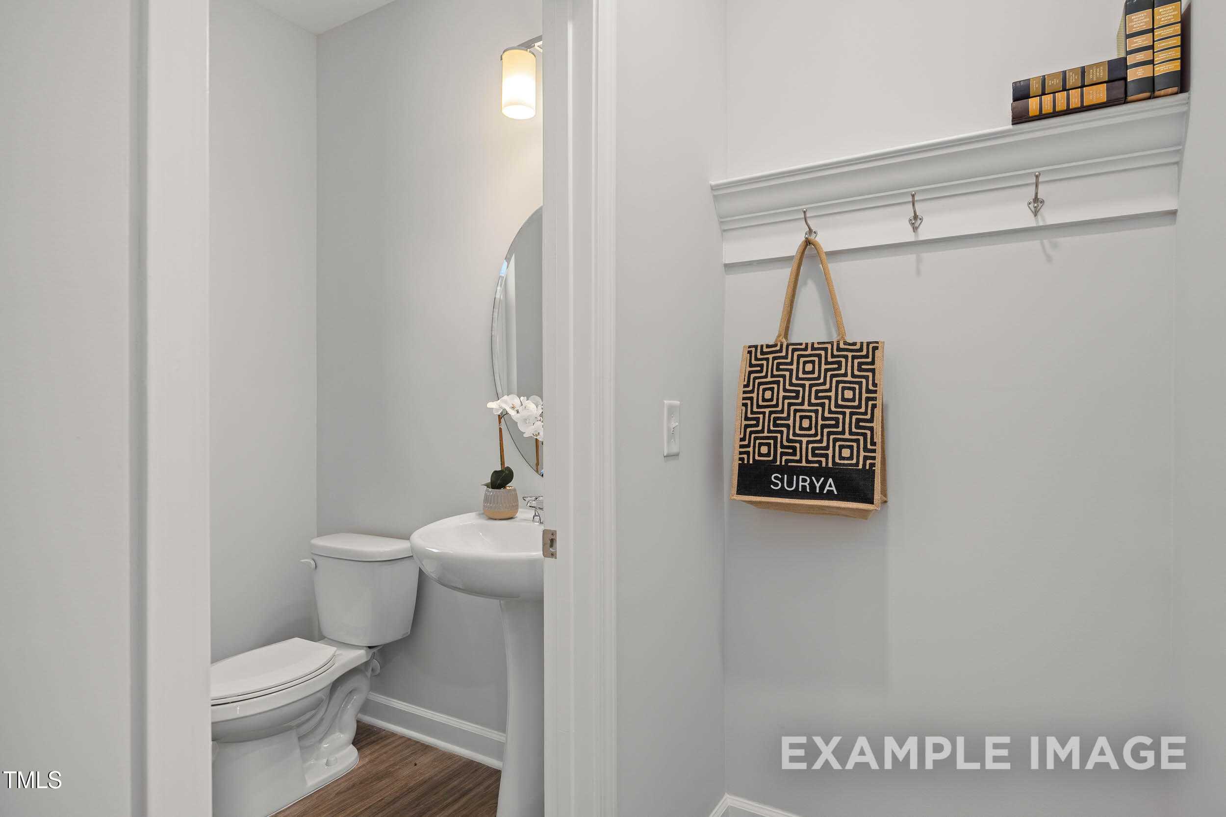 Bright powder room with pedestal sink, round mirror, toilet, and wall hooks in Davidson Homes The Graham, Fuquay-Varina, NC