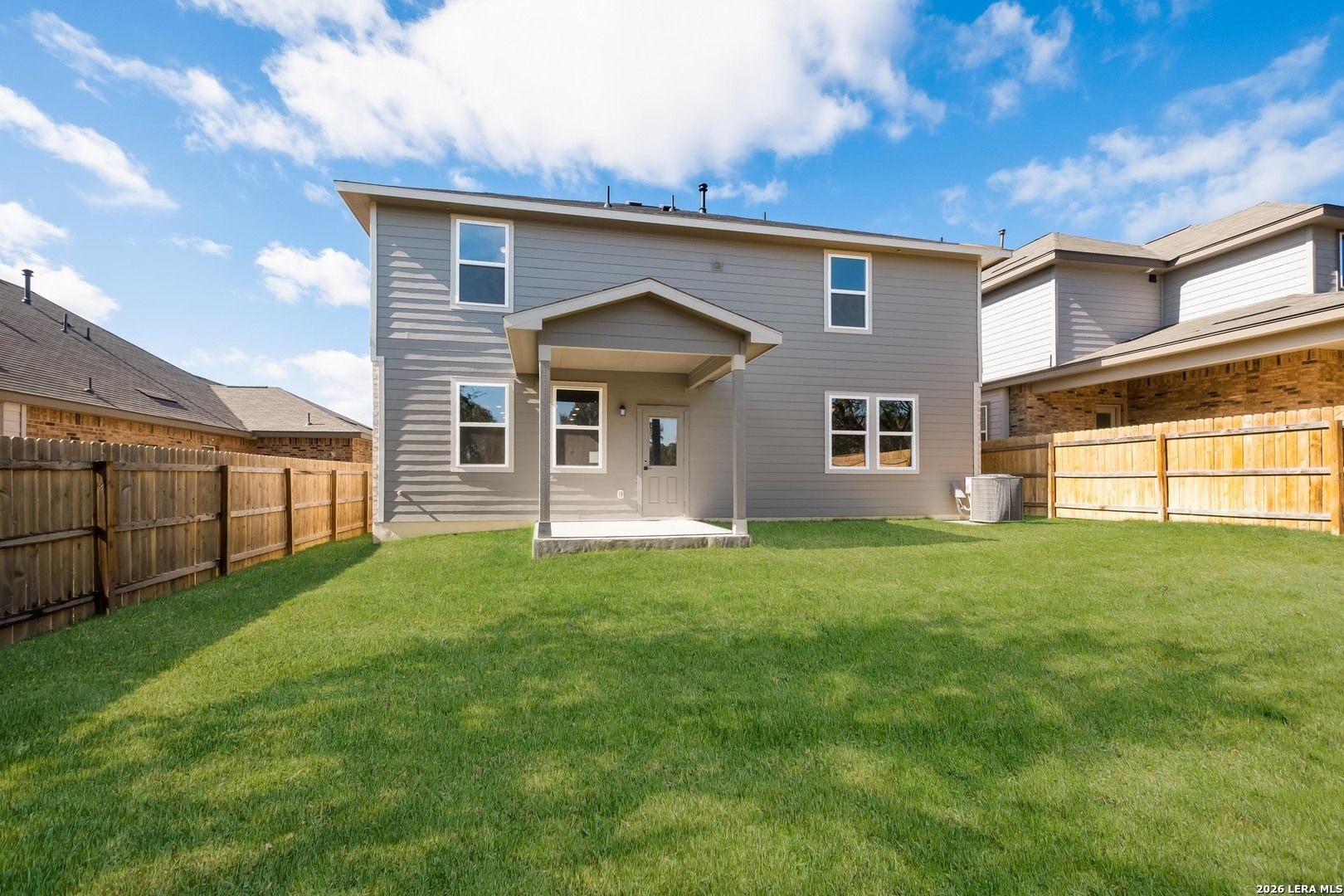 Rear view of two-story Douglas E home featuring covered patio and expansive grassy backyard in Bricewood, San Antonio