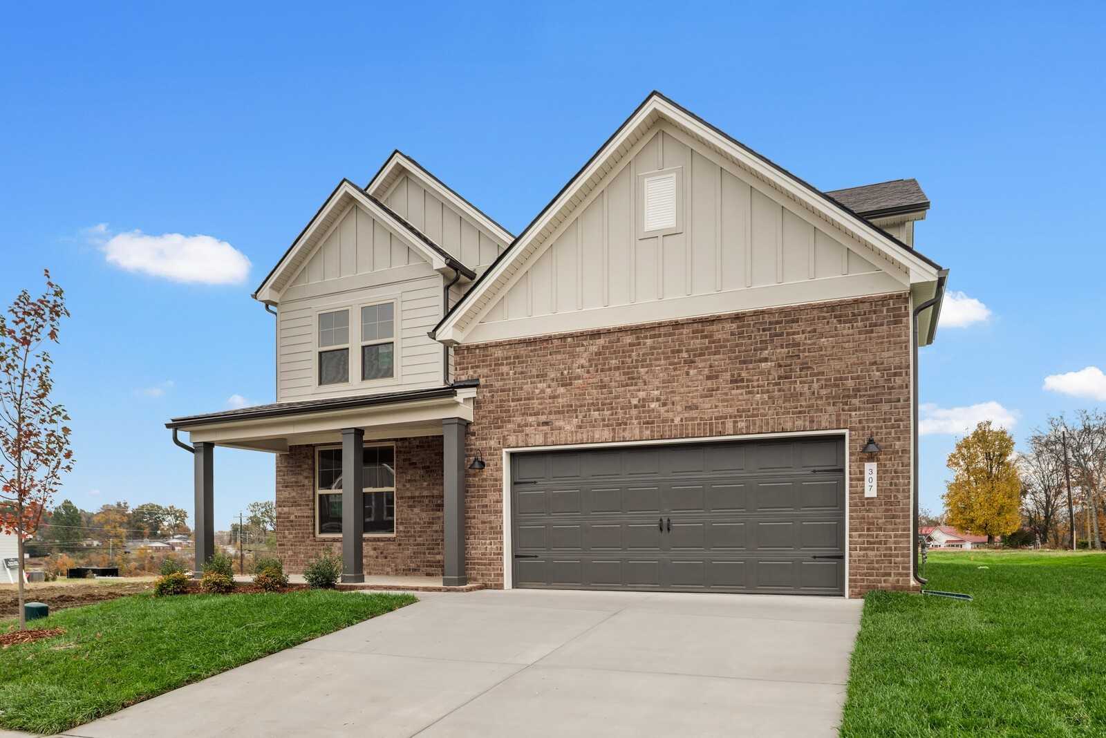 Modern two-story home with beige siding, brick base, 2-car garage, covered porch, and lush lawn in Woods Crossing, Gallatin, Tennessee