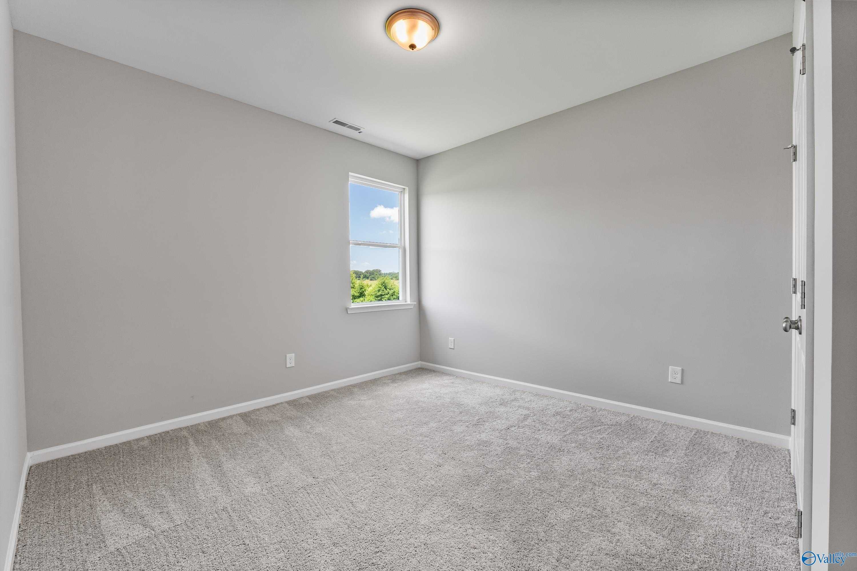 Cozy bedroom with gray walls, plush carpet, and sunny window view in Davidson Homes The Sanctuary, Huntsville, Alabama