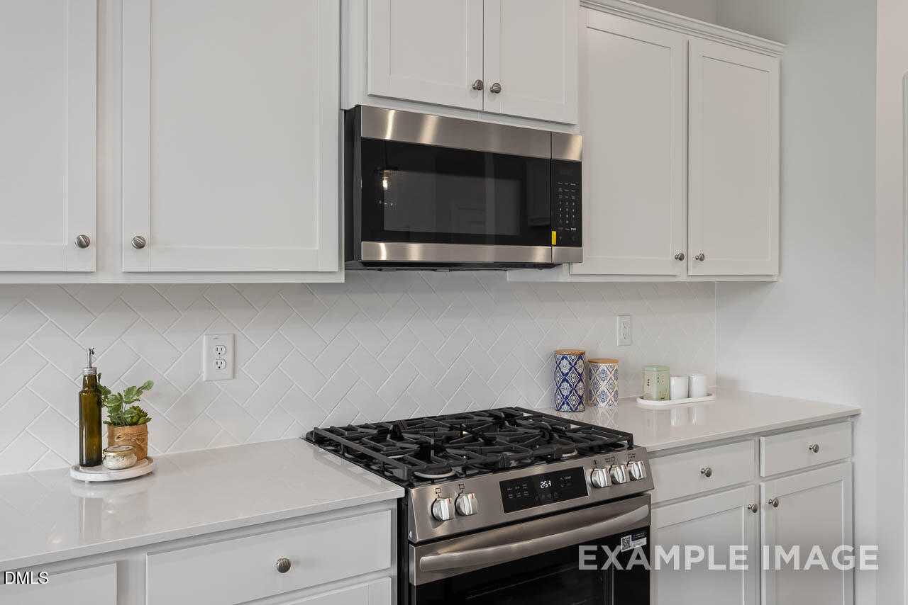 Modern white kitchen with stainless steel gas range, oven, and microwave in Davidson Homes The Warren floor plan, Fuquay-Varina, NC