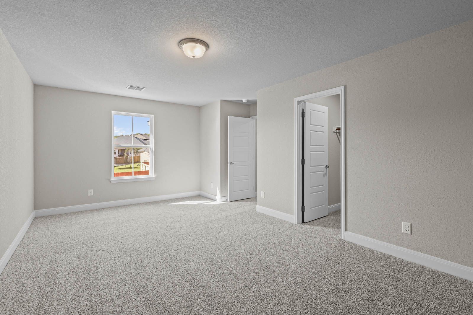 Spacious bedroom in The Jennings G featuring neutral carpet, natural light, and a walk-in closet in Castroville, Texas.