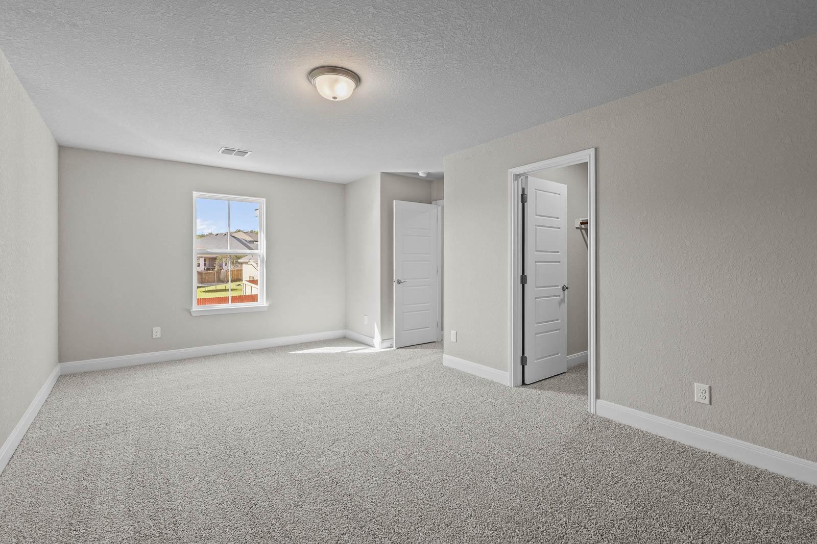 Spacious bedroom in The Jennings G featuring neutral carpet, natural light, and a walk-in closet in Castroville, Texas.