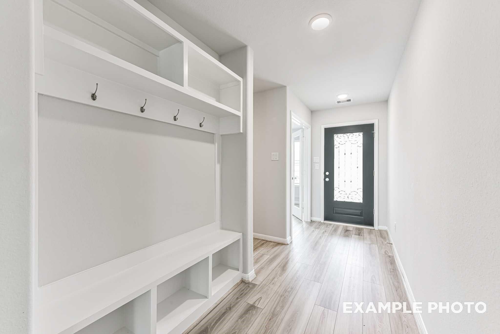 Modern mudroom with white built-in cabinetry, coat hooks, bench, and hallway in Davidson Homes The Riviera A, Rosharon, Texas