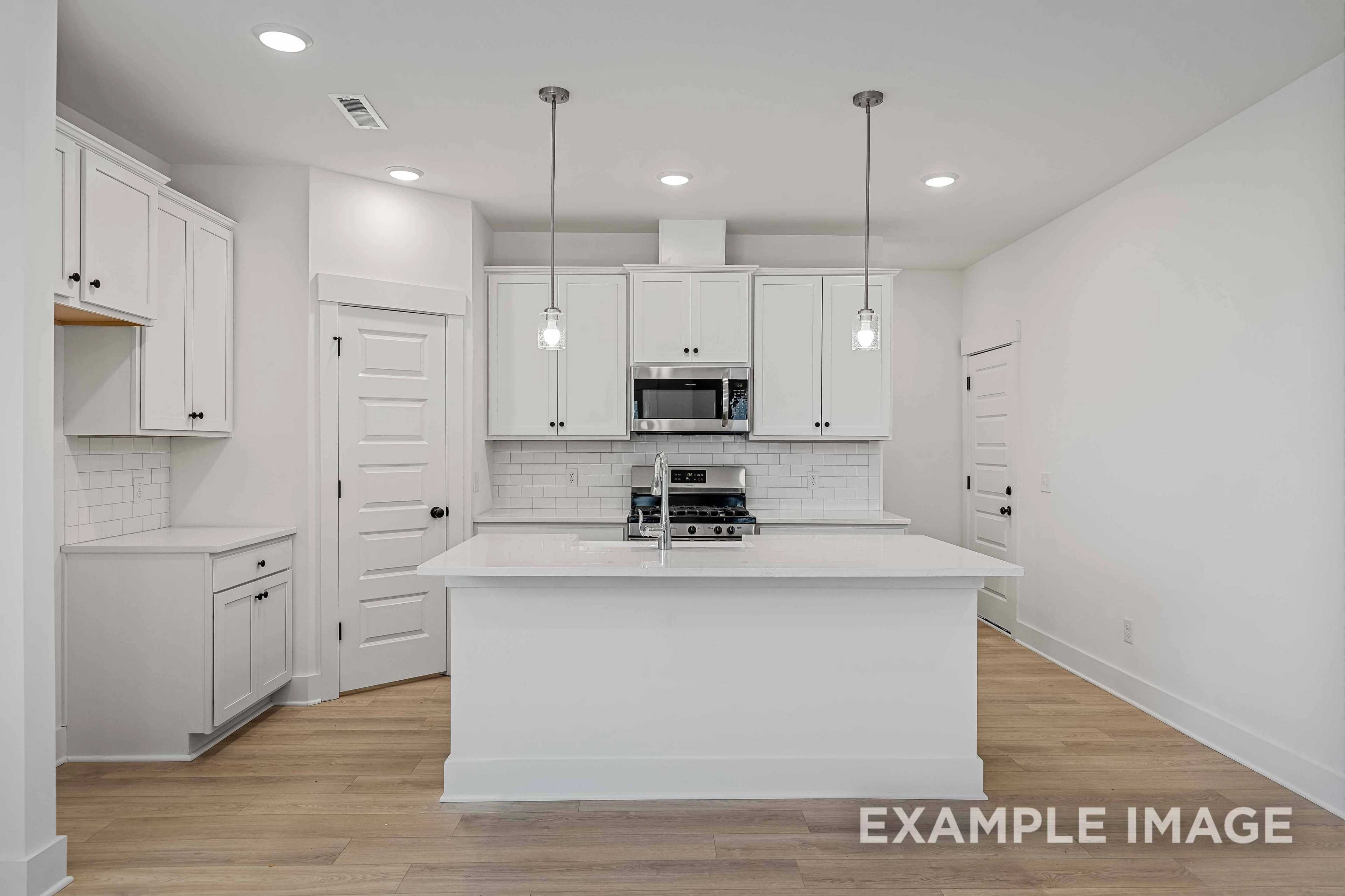Spacious white kitchen in The Charleston with large island, stainless appliances, subway tile backsplash