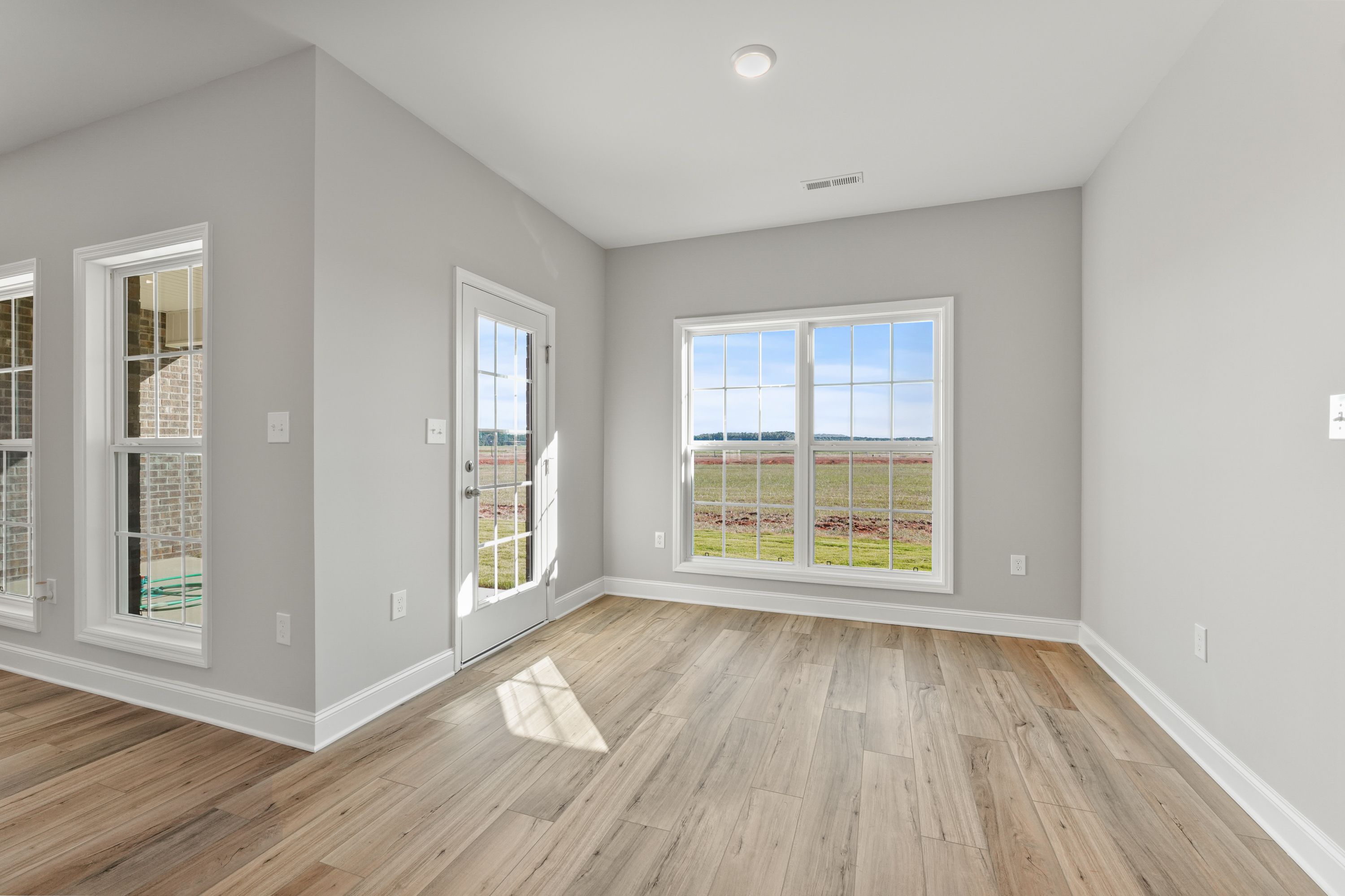 Bright sunroom in The Valencia home with gray walls, hardwood floors, French doors, and panoramic green field views