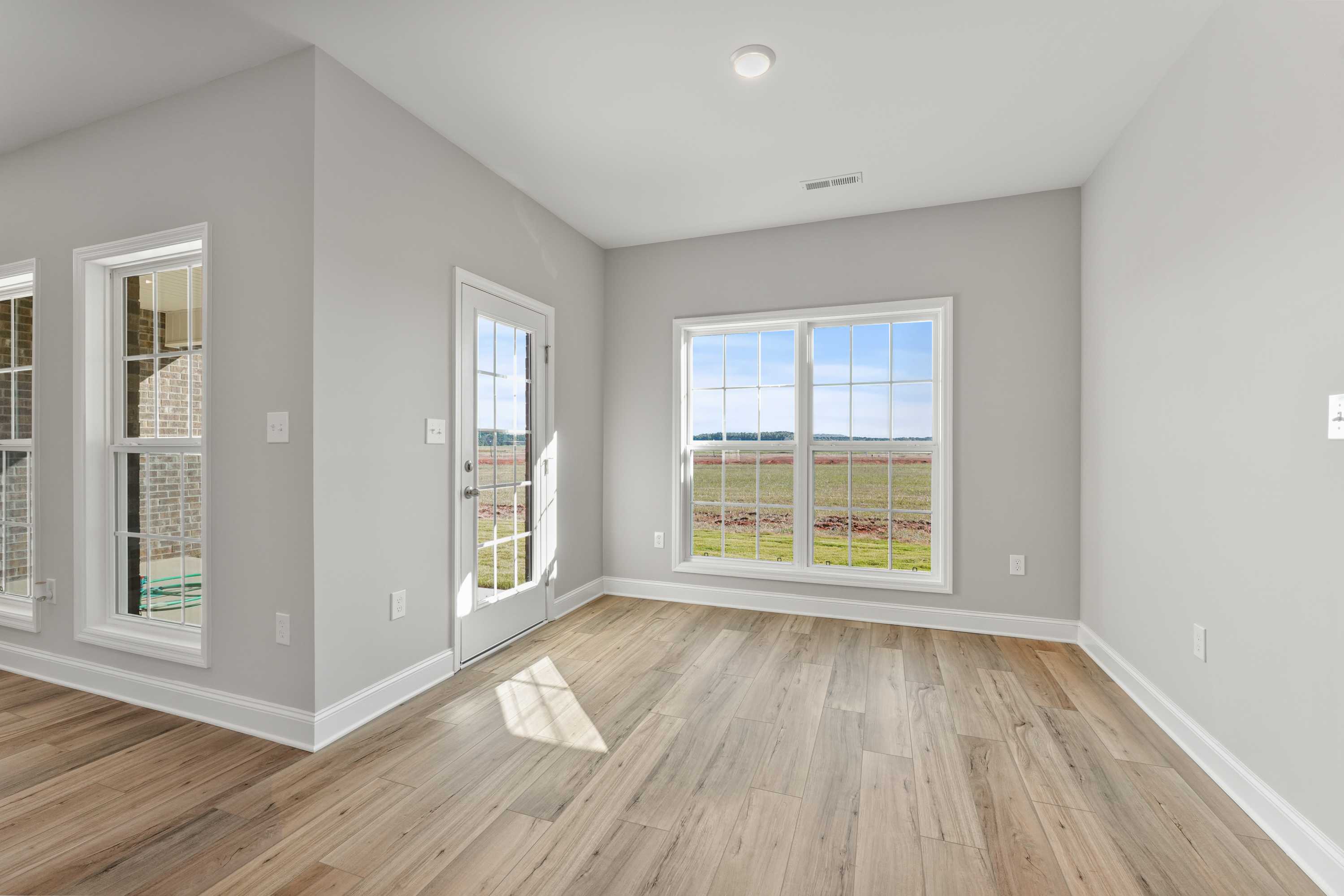 Bright sunroom in The Valencia home with gray walls, hardwood floors, French doors, and panoramic green field views