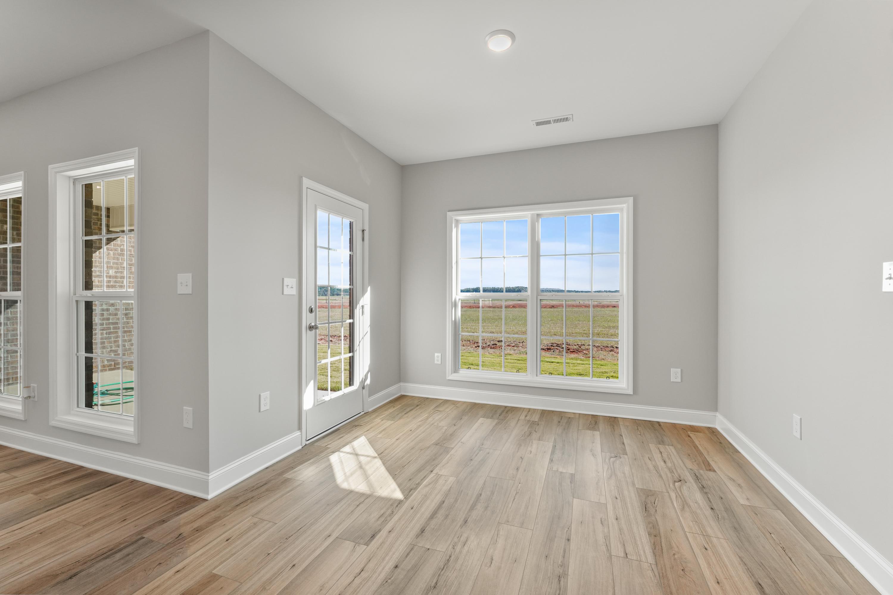 Bright sunroom in The Valencia home with gray walls, hardwood floors, French doors, and panoramic green field views