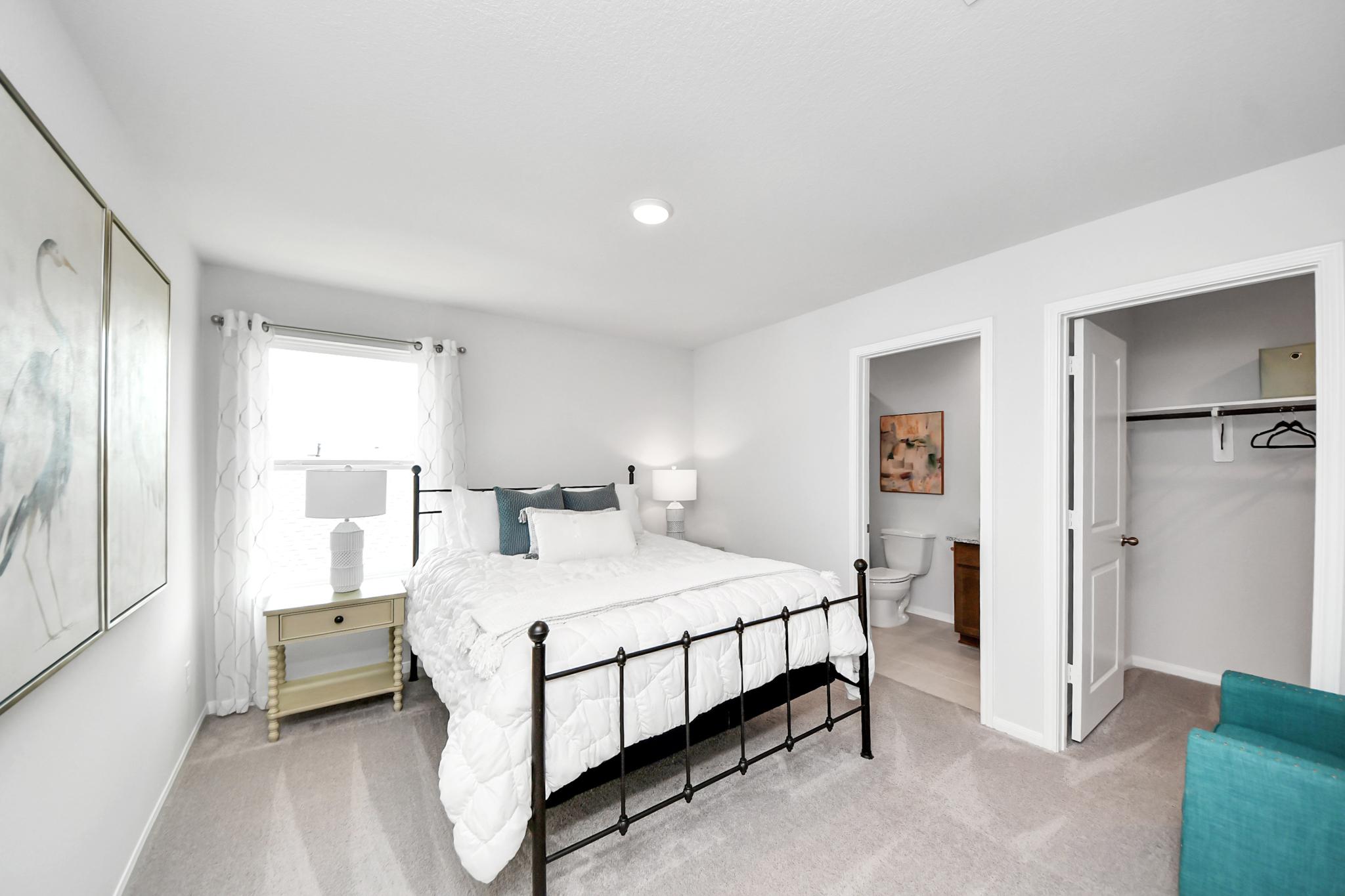 Cozy bedroom in a Sunterra home by Davidson Homes in Katy, Texas, featuring a metal bed frame, ensuite bath, and walk-in closet.