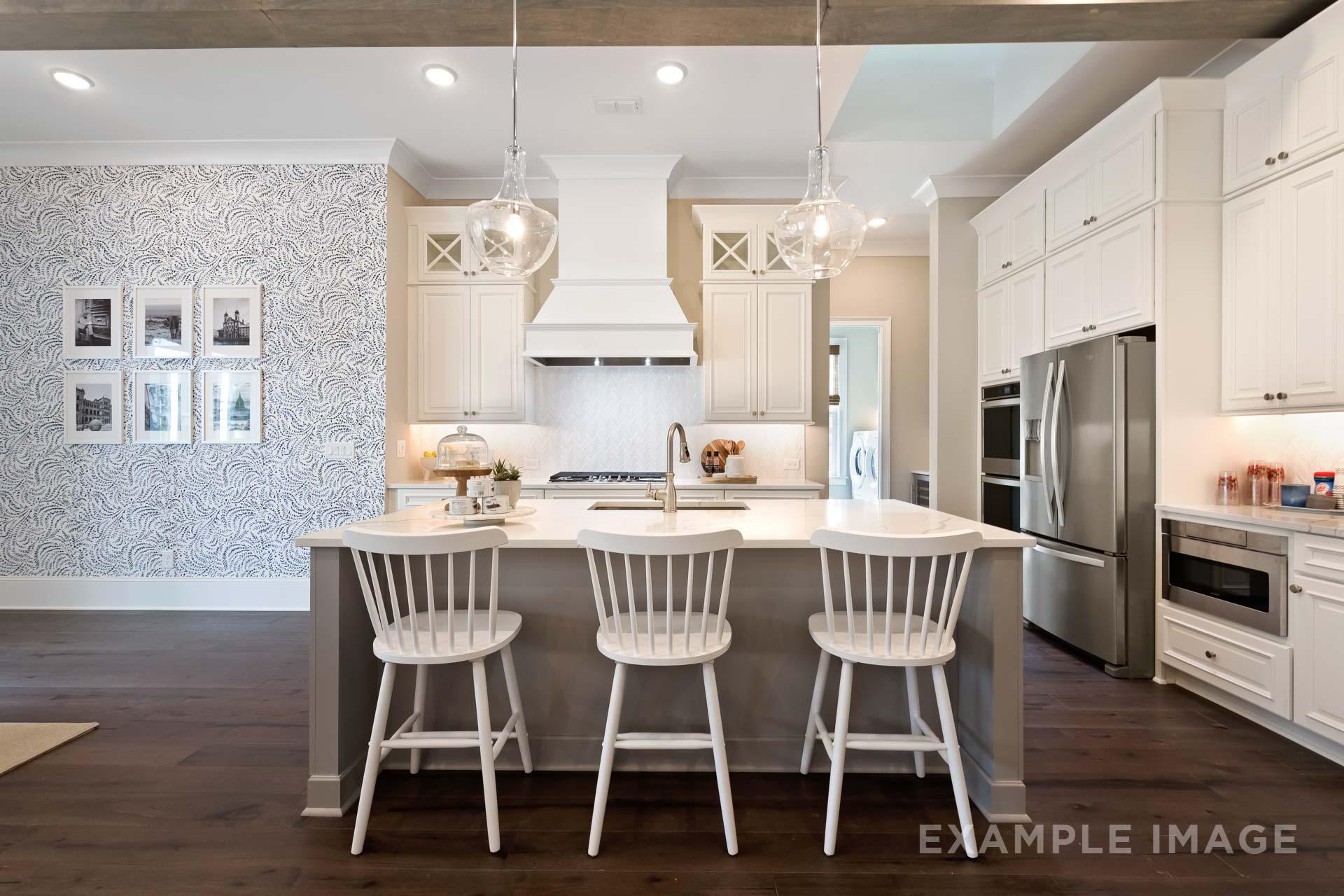 Gourmet kitchen in The Seaside with white shaker cabinets, gray island, stainless appliances, and pendant lights
