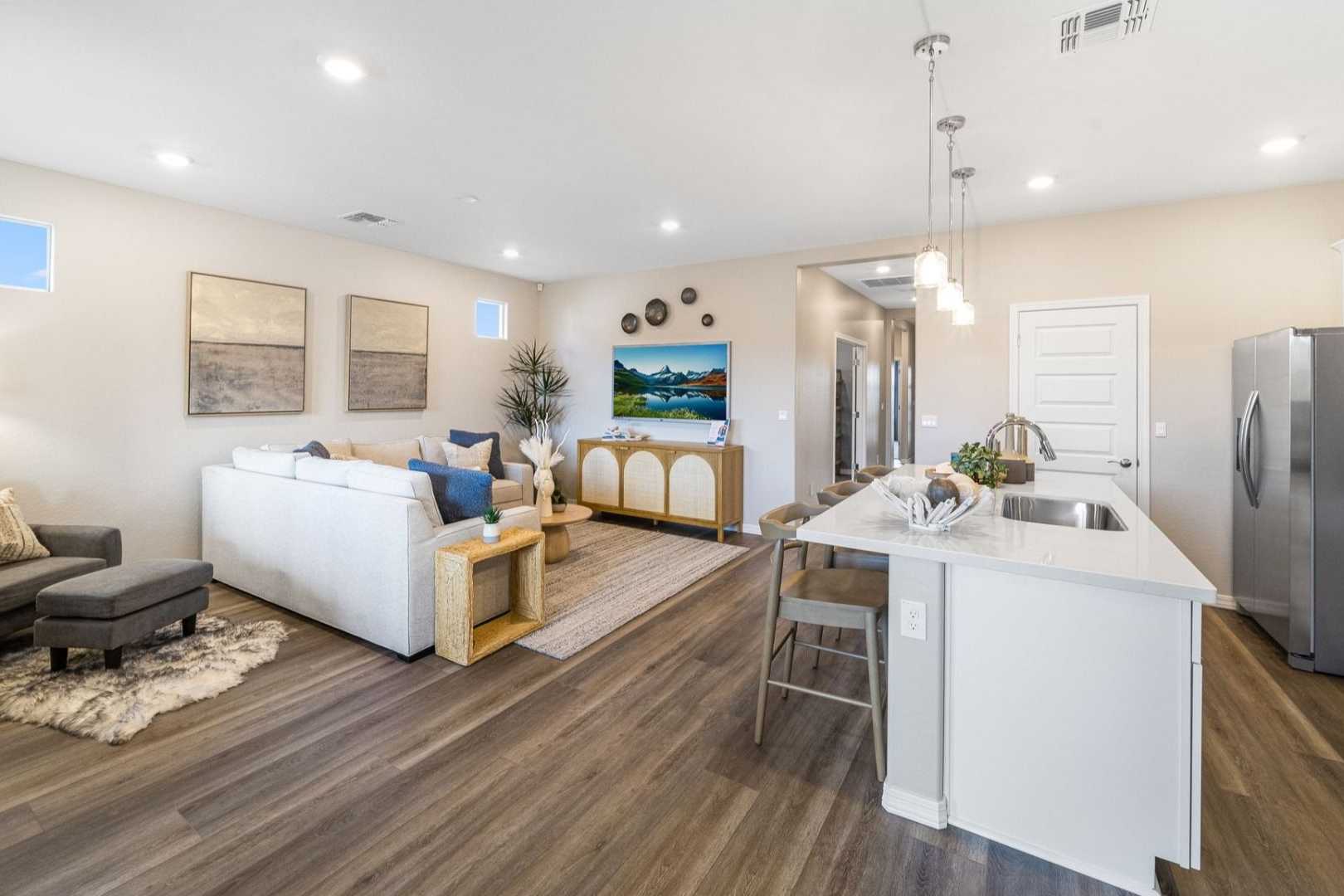 Open-concept living room and kitchen at South Ranch in Prescott AZ featuring hardwood floors, white island, sofa, and pendant lights