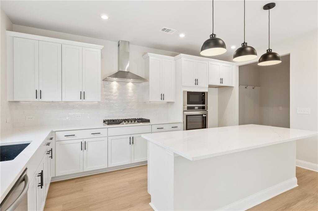 Spacious modern white kitchen with quartz island, stainless appliances, subway tile backsplash in The Hickory B, Buford GA