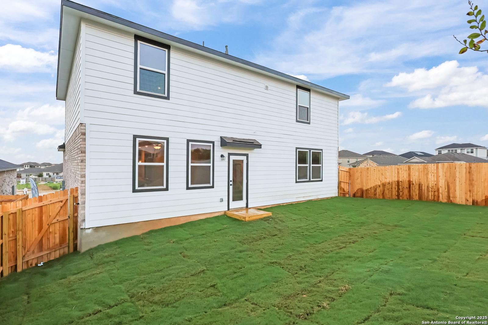Two-story white exterior with covered back patio, lush green yard, and privacy fence in Davidson Homes The Douglas F, Comanche Ridge, San Antonio