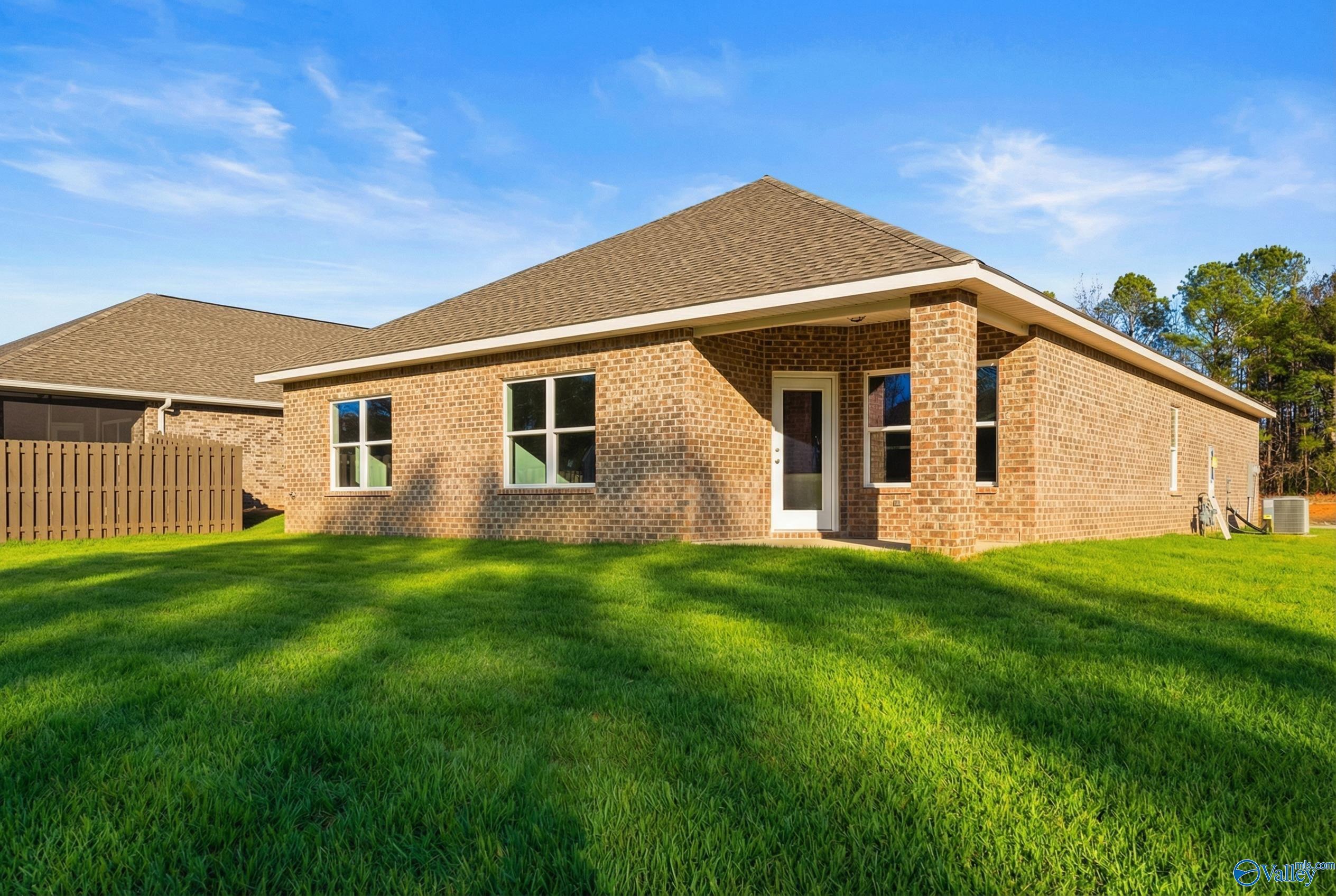 Brick single-story home with 2-car garage, large windows, lush green lawn, and backyard fence in The Highlands, Arab, Alabama