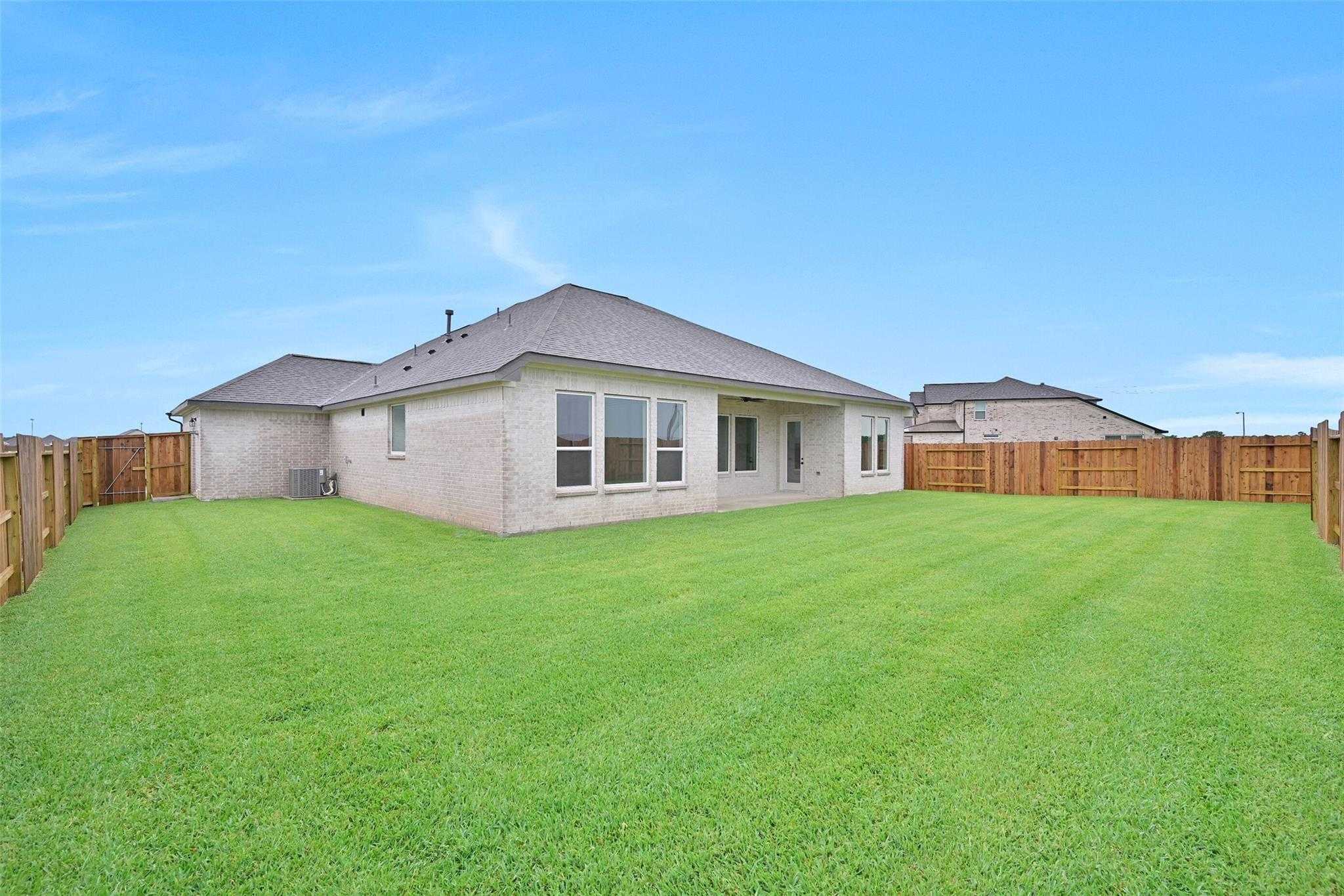 Backyard of Davidson Homes The Edward C 3-car garage home with covered patio, large windows, lush green lawn, and wooden fence in Lago Mar, Texas City