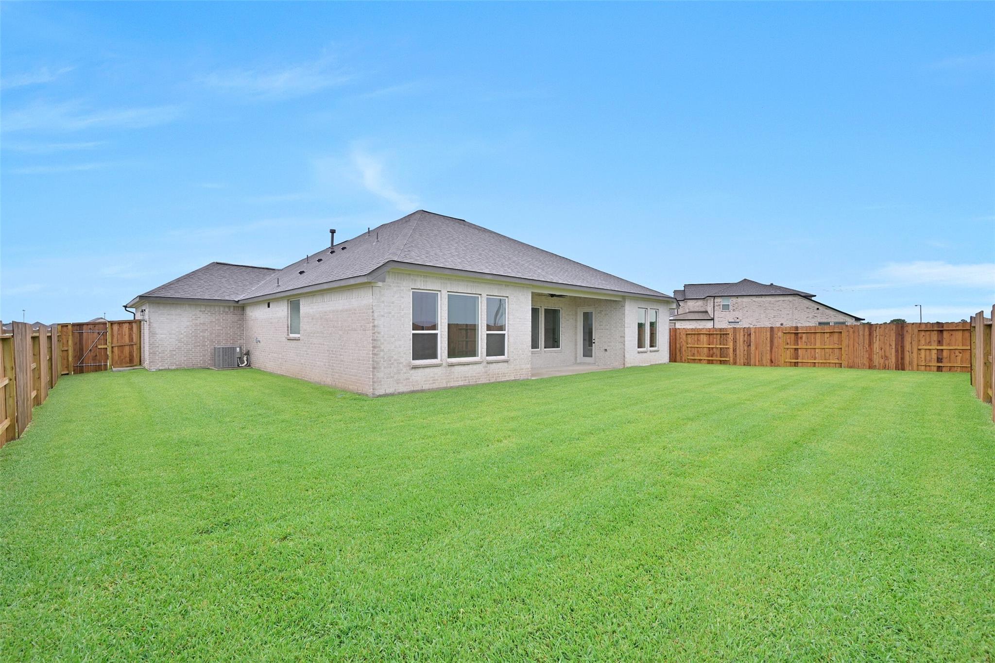 Rear view of single-story beige home with covered patio, sliding doors, lush green lawn, and wooden fence in Lago Mar, Texas City