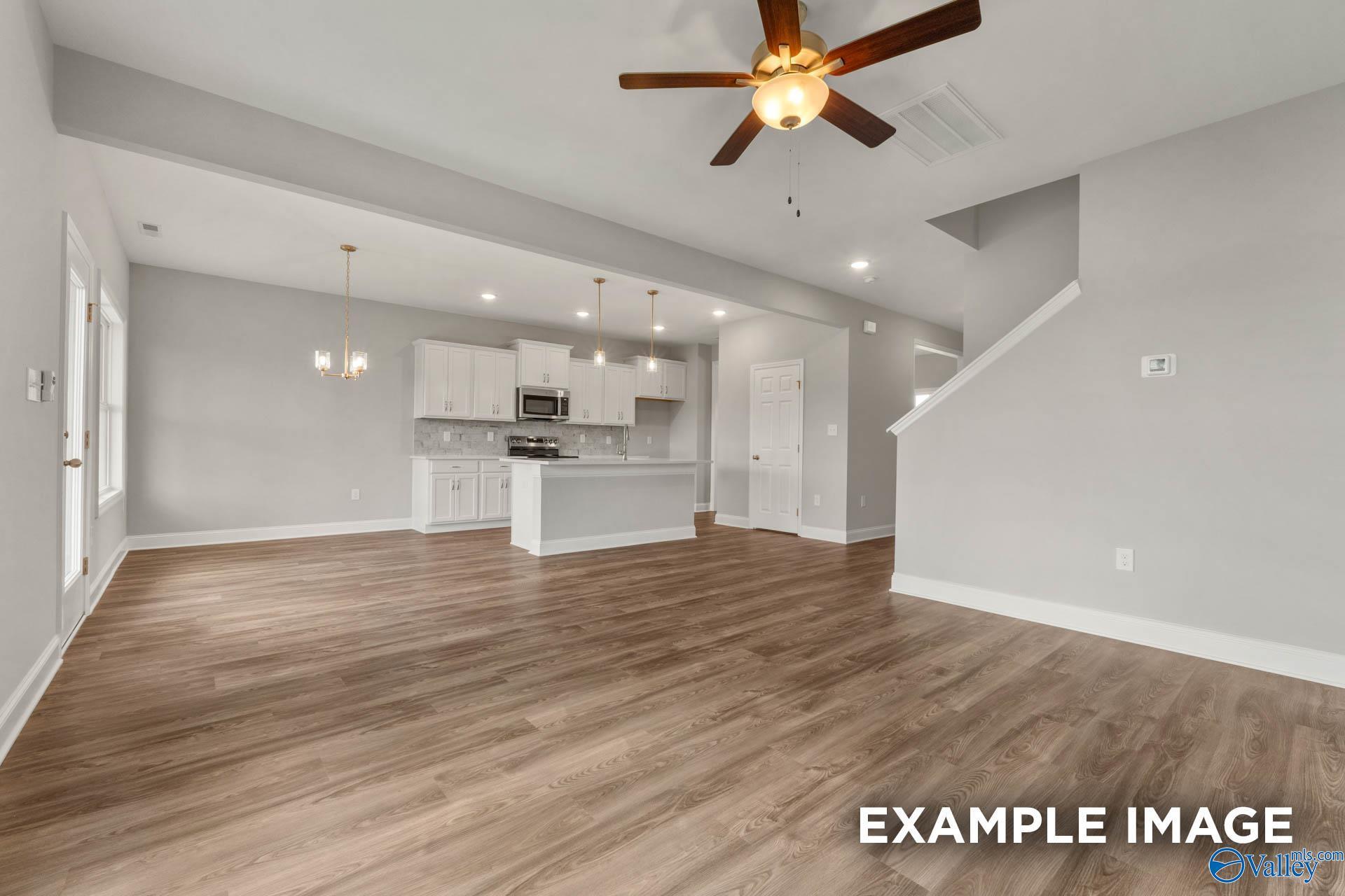 Open-concept great room with white kitchen cabinets, central island, hardwood floors, and staircase in Davidson Homes Shelby B, New Market, AL