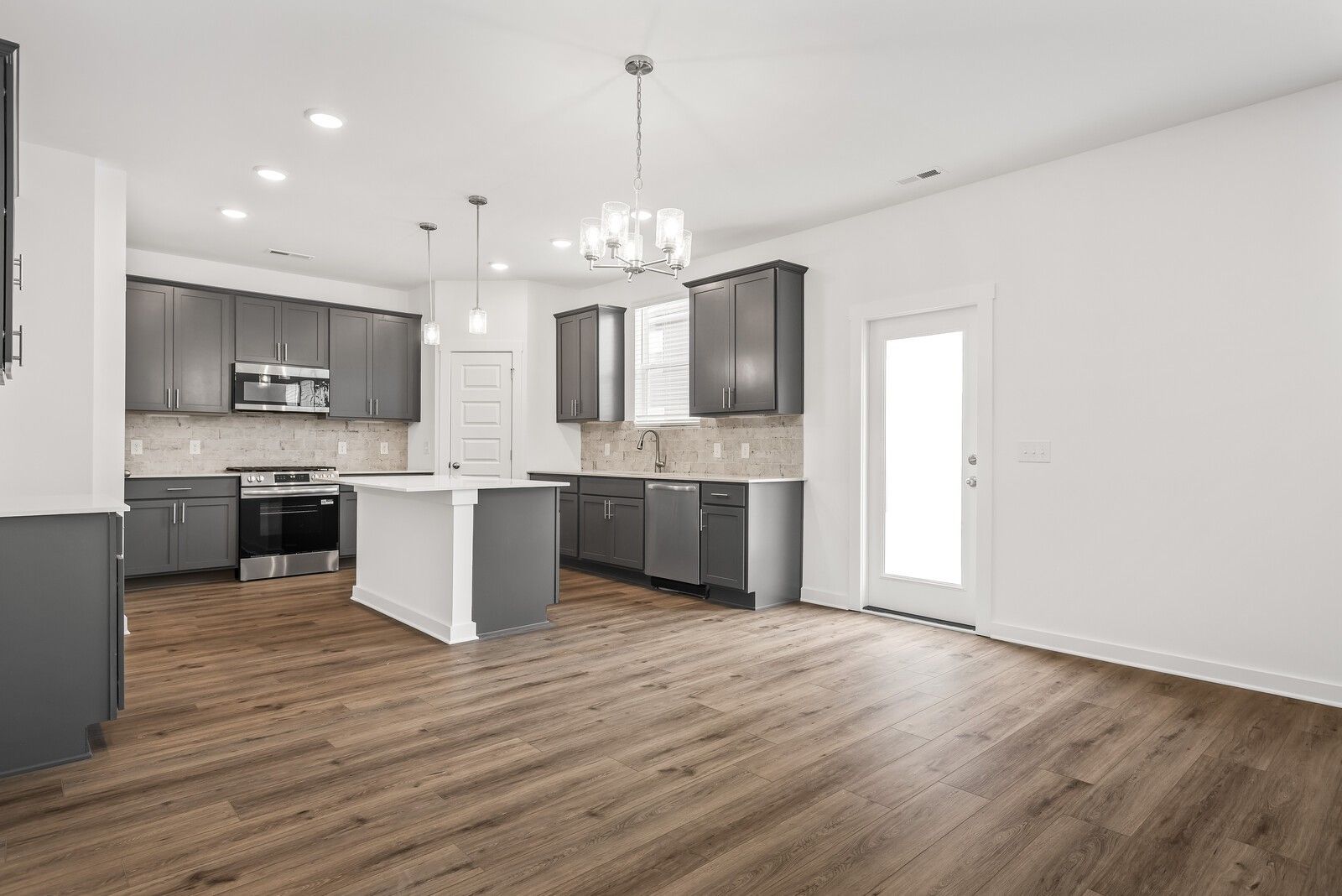 Modern kitchen with gray shaker cabinets, white island, stainless steel appliances, wood floors in Davidson Homes The Gordon C, White House, TN