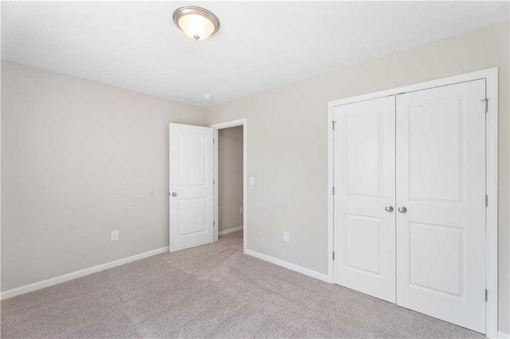 Bright bedroom featuring beige walls, white double closet doors, open bathroom entry, and carpet flooring in Evermore Homes The Washington, Phenix City, Alabama