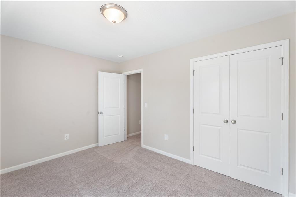 Bright bedroom featuring beige walls, white double closet doors, open bathroom entry, and carpet flooring in Evermore Homes The Washington, Phenix City, Alabama