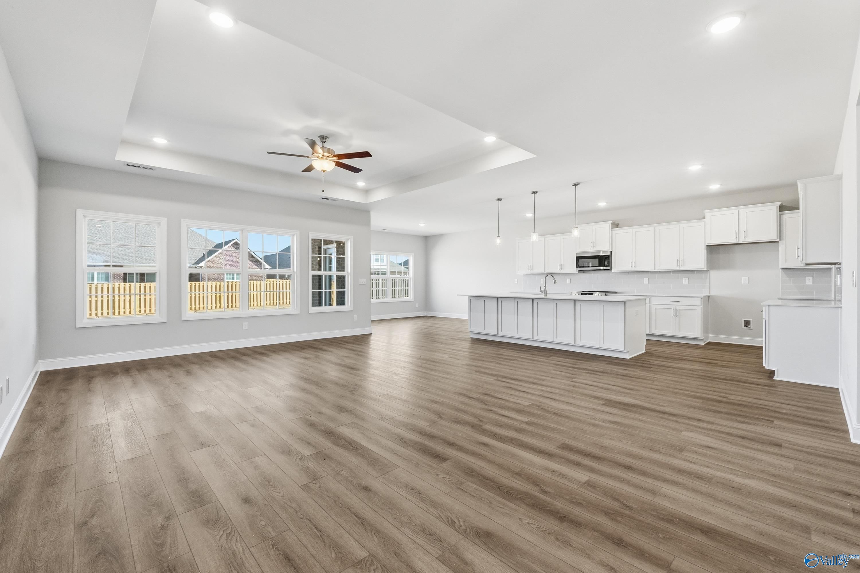 Bright open-concept kitchen and living area with white cabinets, wood floors, ceiling fan, and large windows in Davidson Homes The Finleigh, Harvest, AL