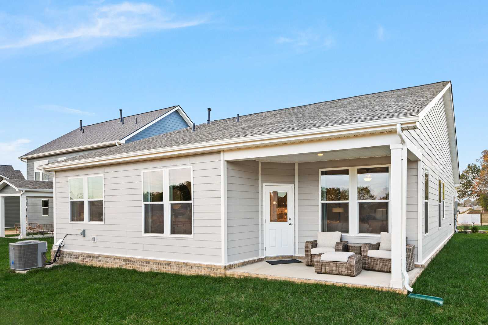Rear view of modern gray-sided home at Sage Farms in White House Tennessee with covered patio and wicker seating