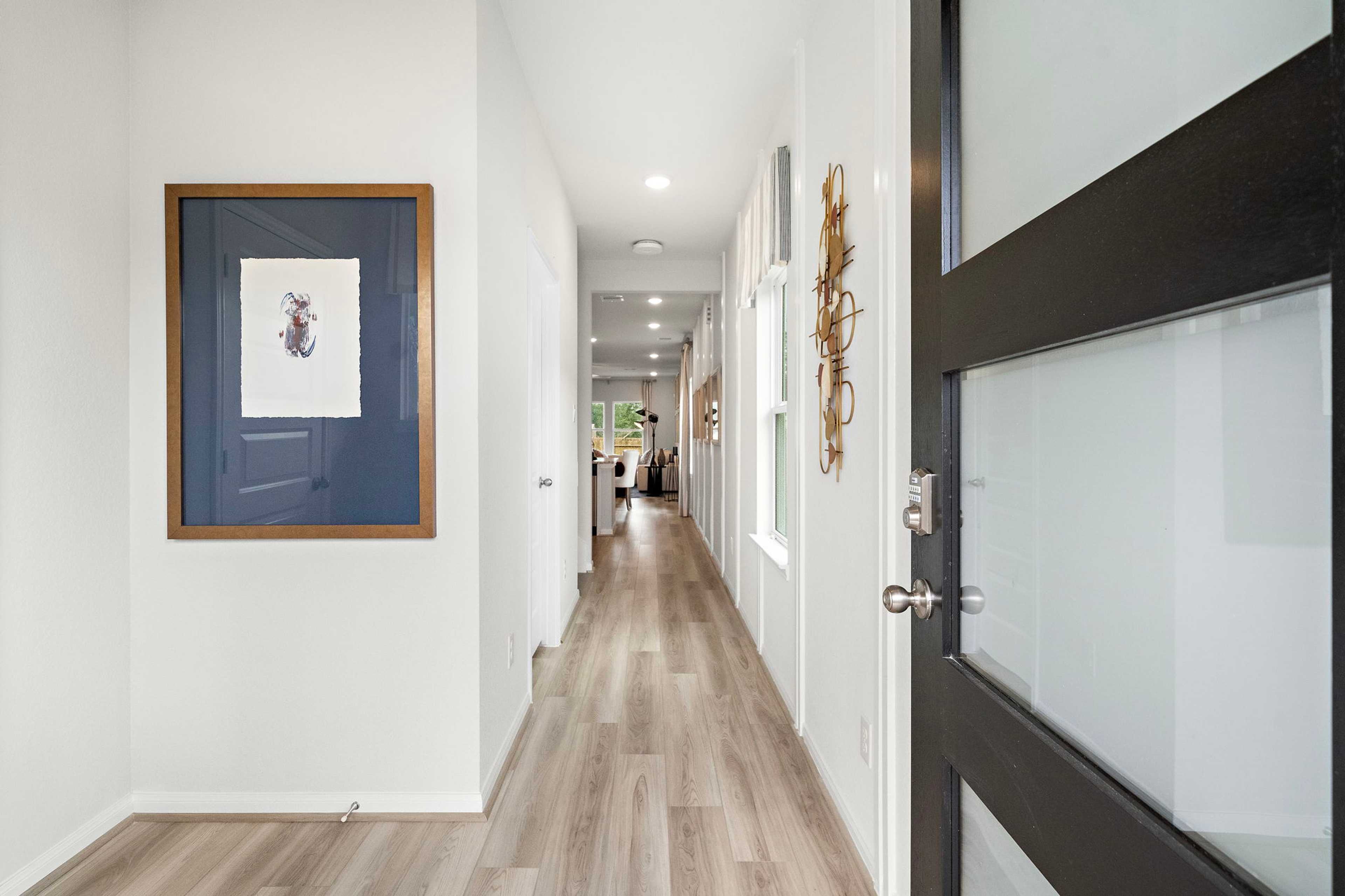 Spacious hallway in Liberty Estates home, Cleveland Texas with hardwood floors, white walls, framed art, and frosted glass door