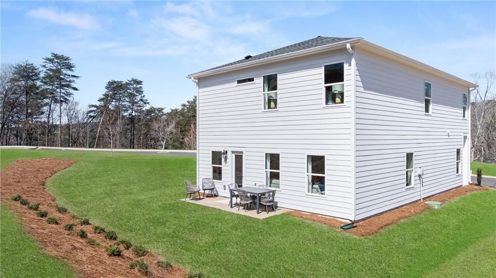 Two-story Craftsman home exterior with covered patio, outdoor seating, white siding, green lawn, and pine trees in The Bluffs, Canton, GA - Davidson Homes The Burton C