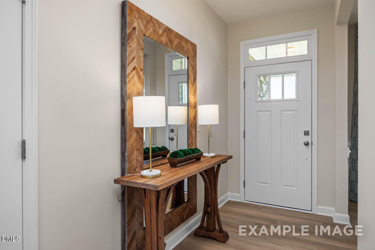Elegant entryway with wooden console table, large framed mirror, lamps, and greenery in The Willow B home, Lillington, NC