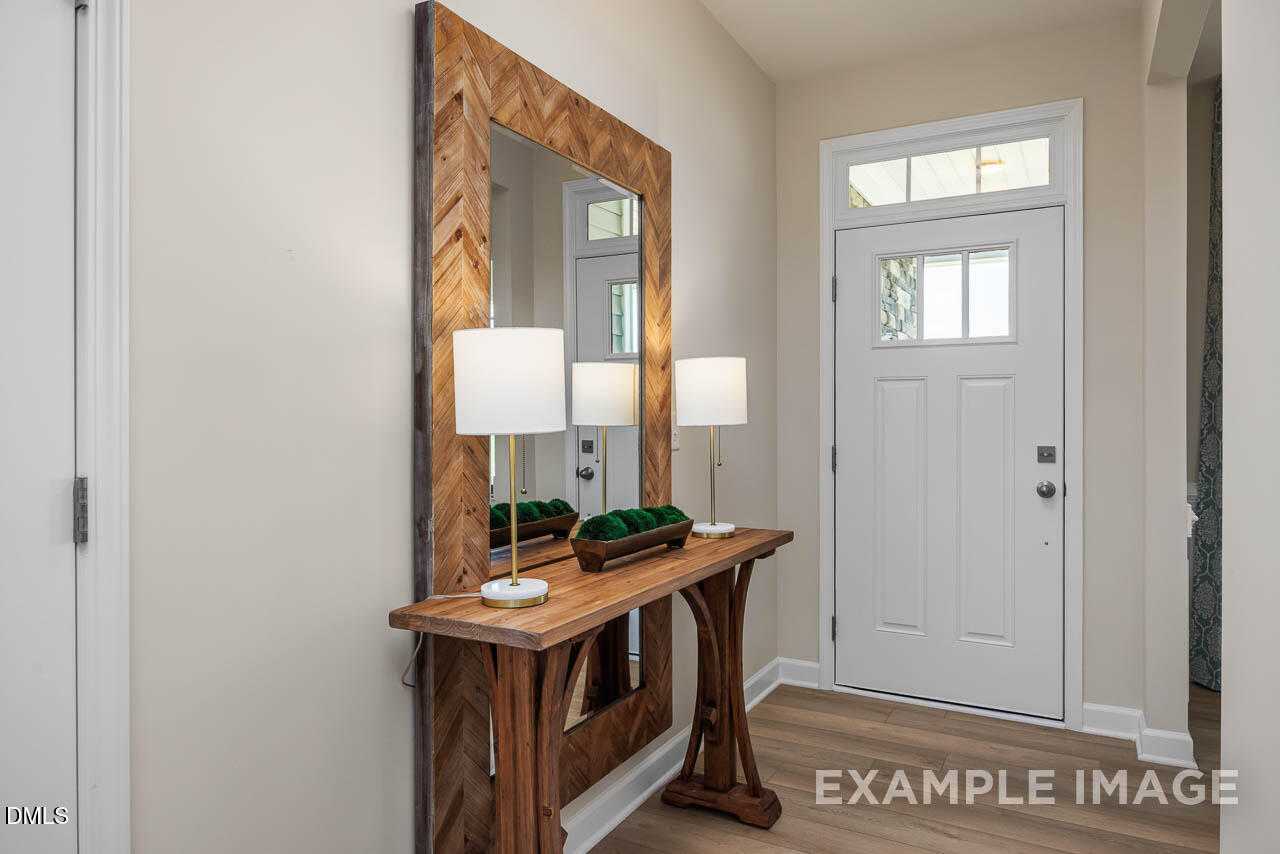 Elegant entryway with wooden console table, large framed mirror, lamps, and greenery in The Willow B home, Lillington, NC