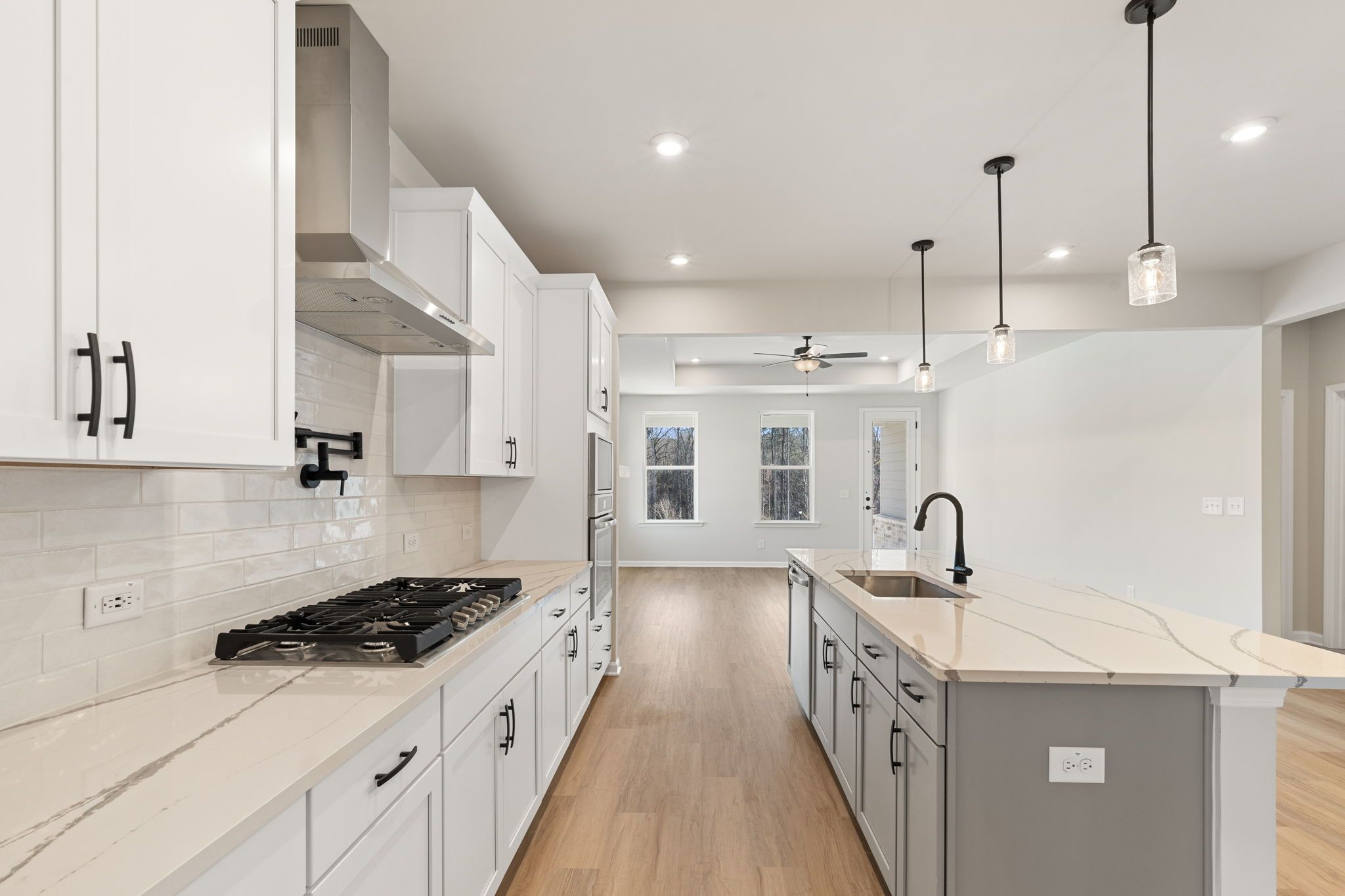 Modern white shaker kitchen with quartz island, gas range, and stainless hood in Davidson Homes The Glenwood C, Loganville, GA