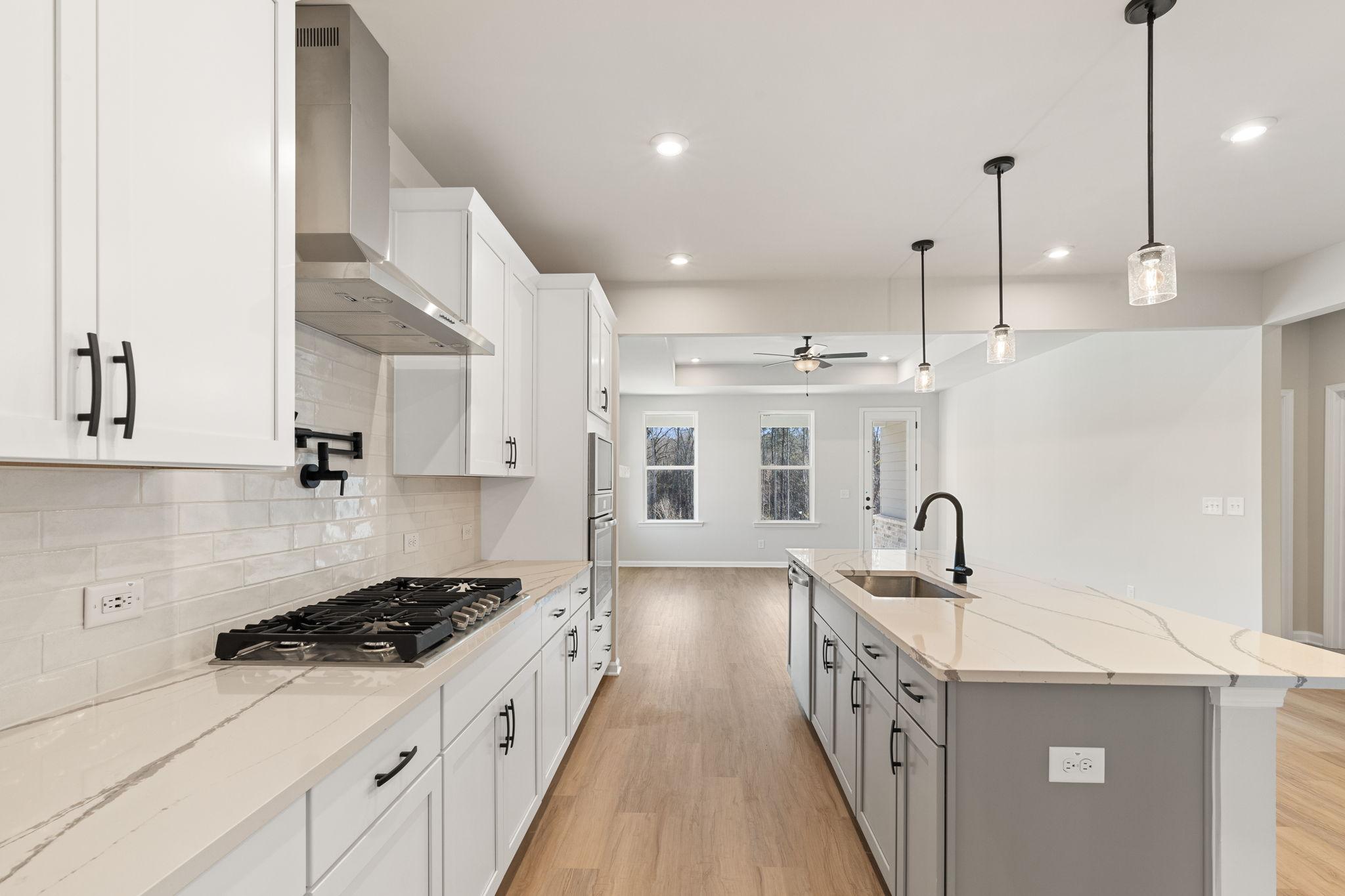 Modern white shaker kitchen with quartz island, gas range, and stainless hood in Davidson Homes The Glenwood C, Loganville, GA